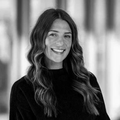 Black and white portrait of a smiling woman with long wavy hair wearing a dark top.
