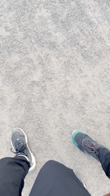Two people wearing athletic shoes standing on a sandy surface, viewed from above.