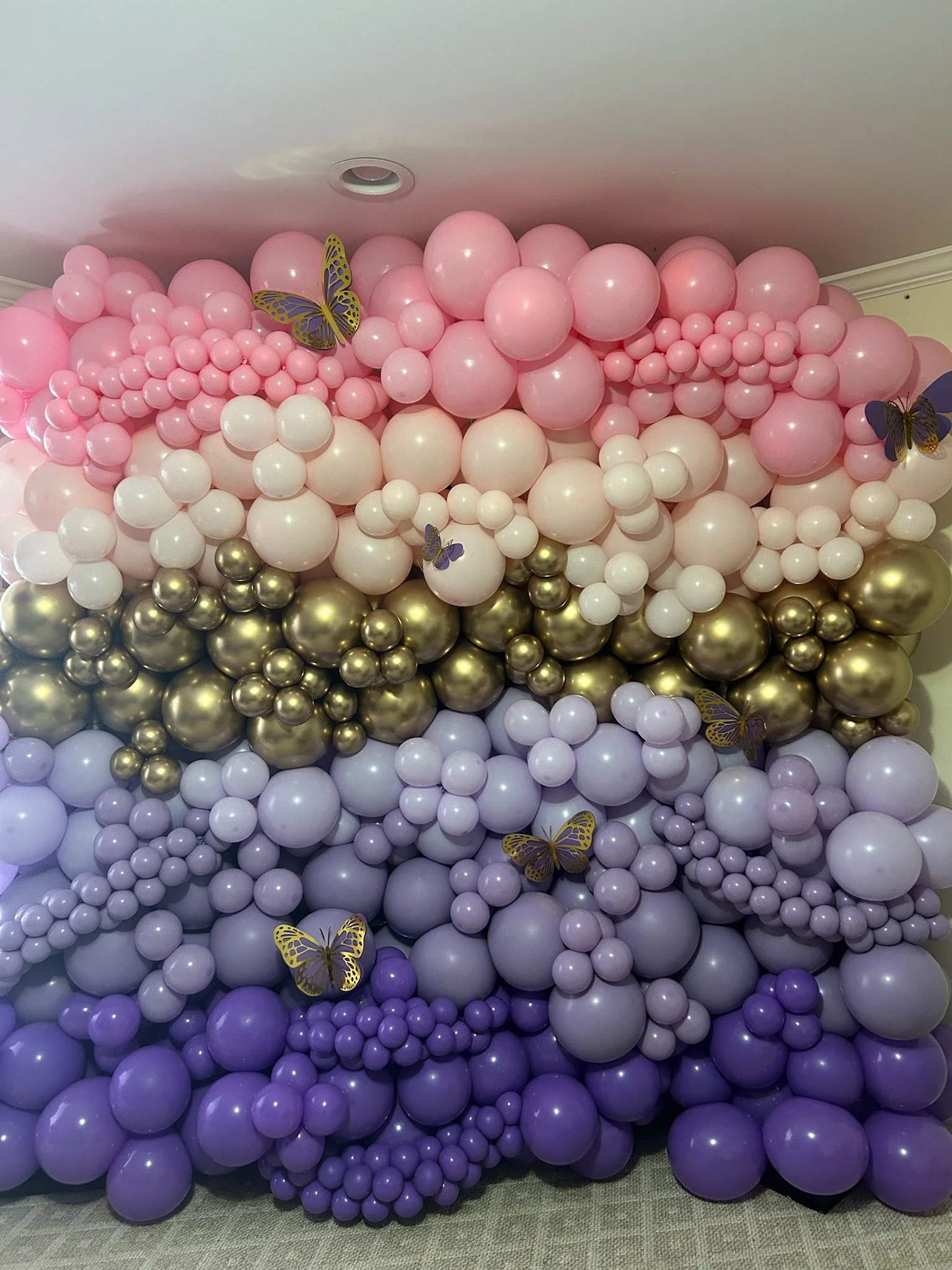 Arrangement of pink, white, purple, and gold balloons with decorative purple and yellow butterflies.