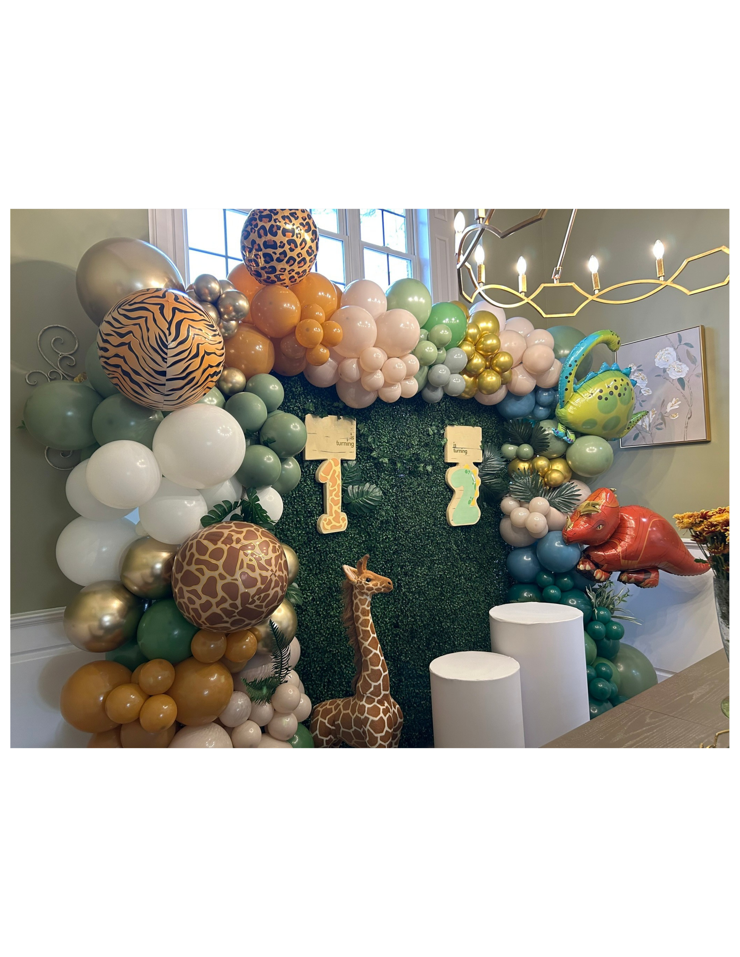 Decorative backdrop with balloons, greenery, and animal-themed decorations for a birthday celebration, featuring giraffe and dinosaur balloons and the number 123.