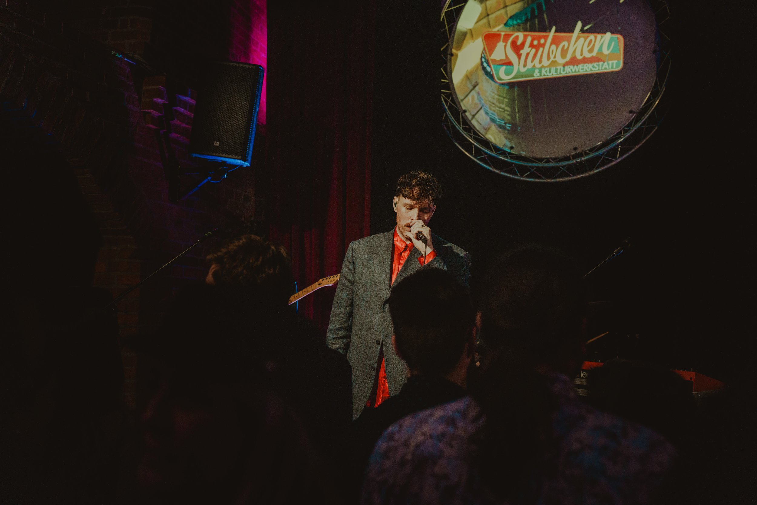 singer on stage in front of colorful background, low angle photographed from concert guests perspective, people in foreground