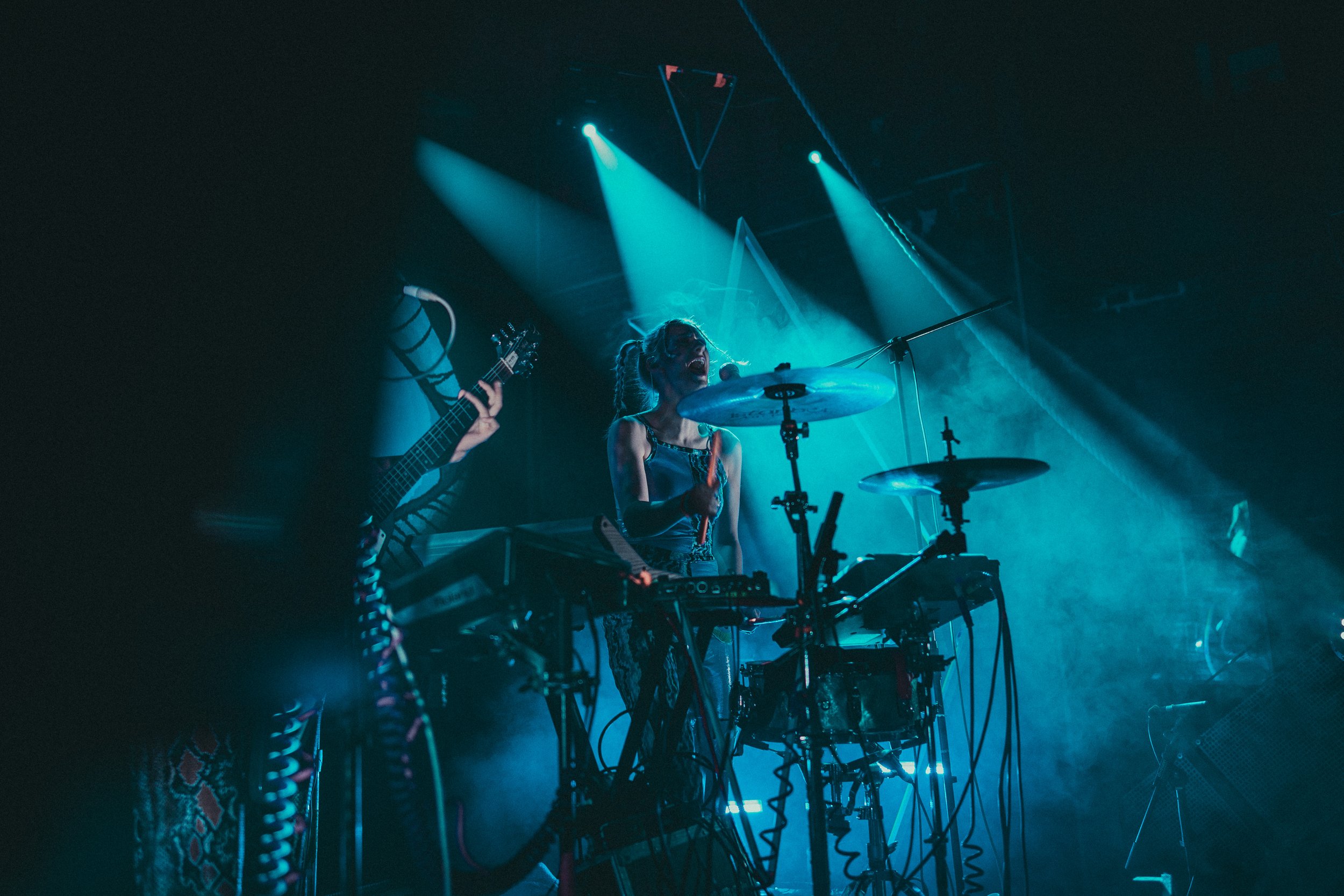 Female drummer on stage, laughing and enjoying music, covered by blue light