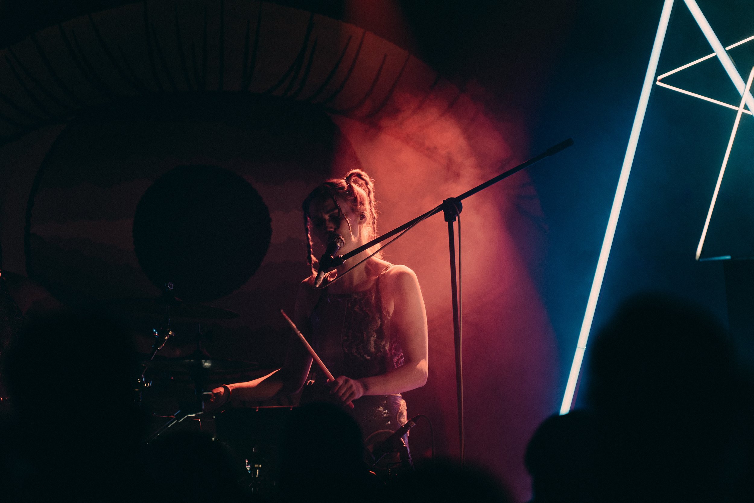 female drummer, singing on a dark foggy stage in spotlight