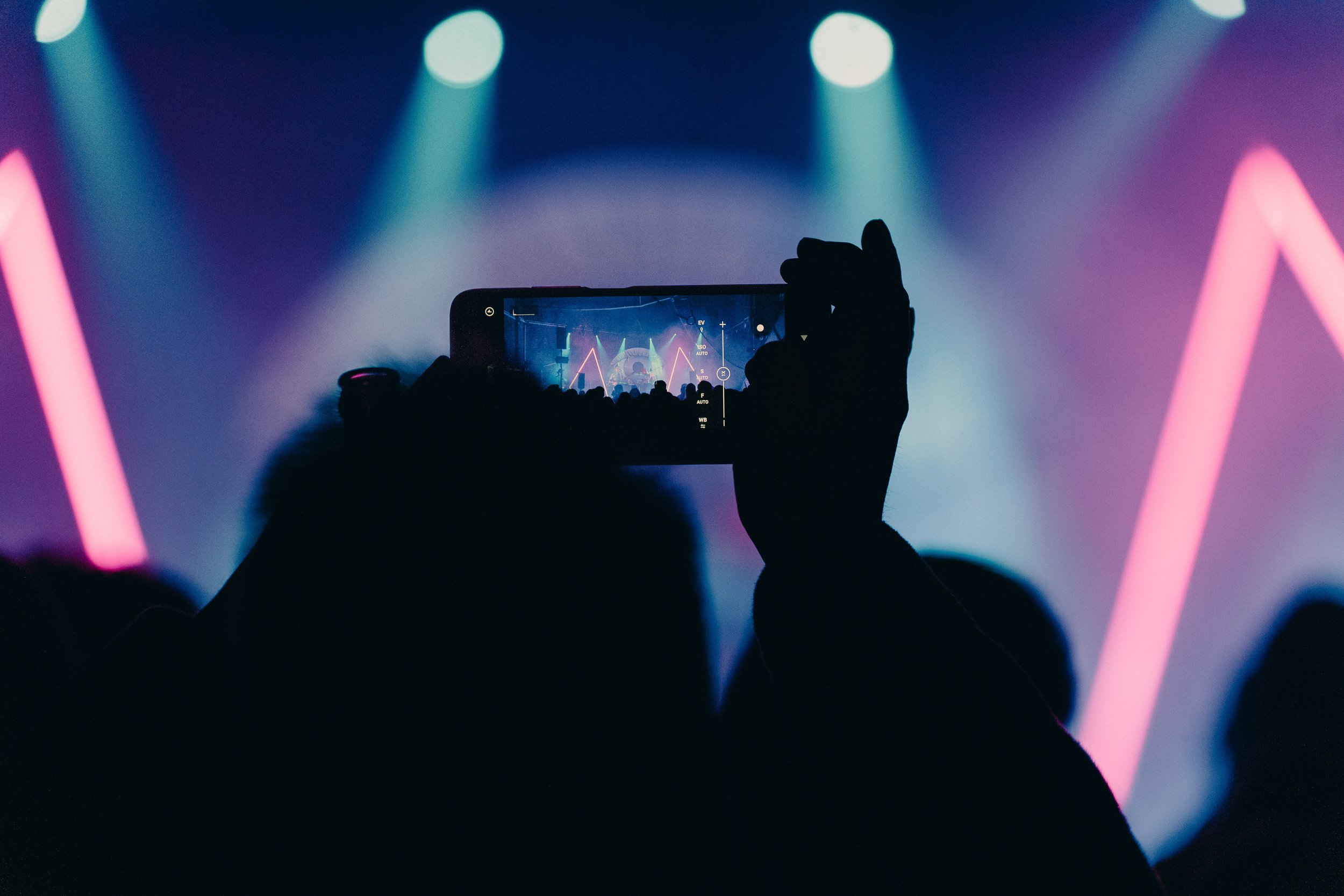 someone taking a photo with a phone of a stage covered in colorful lights