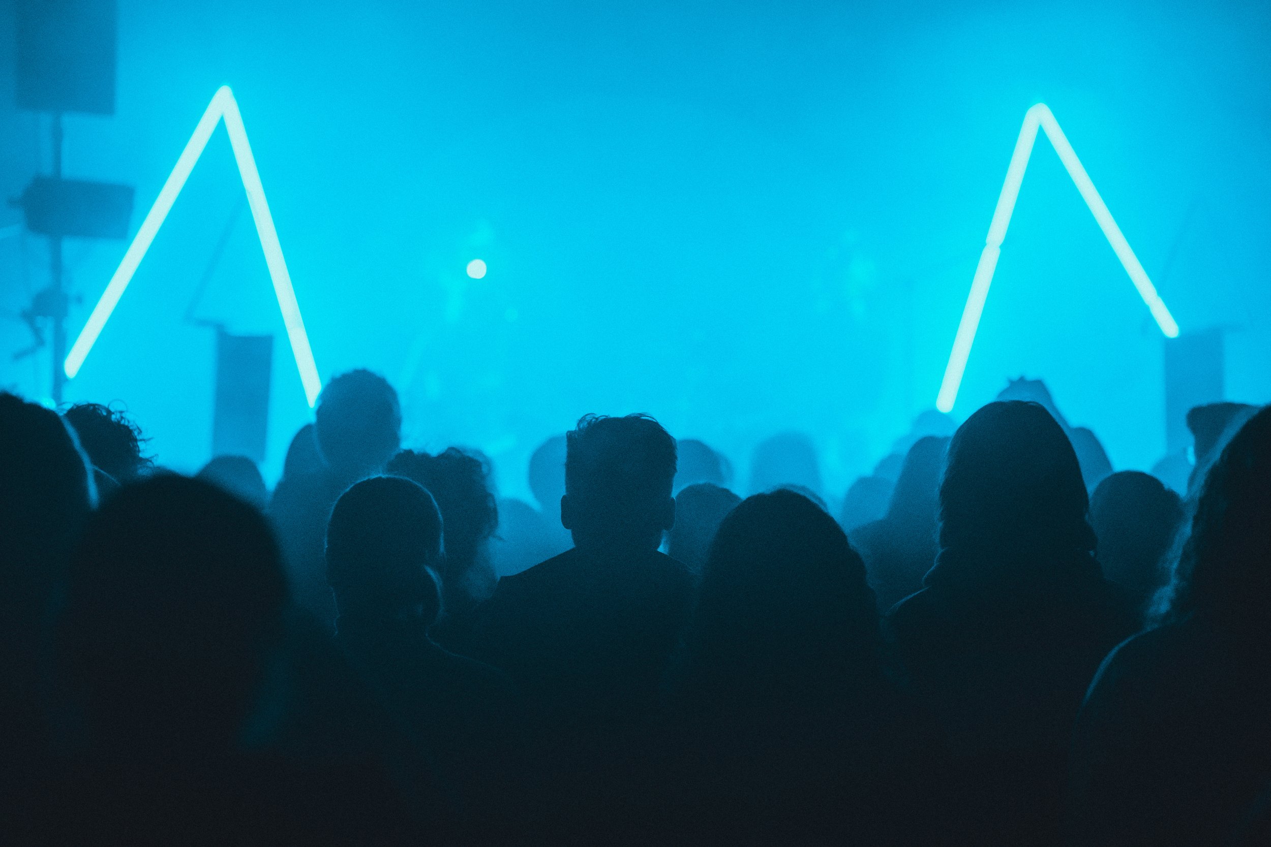 group of people in front of a stage with two blue triangles enjoying music