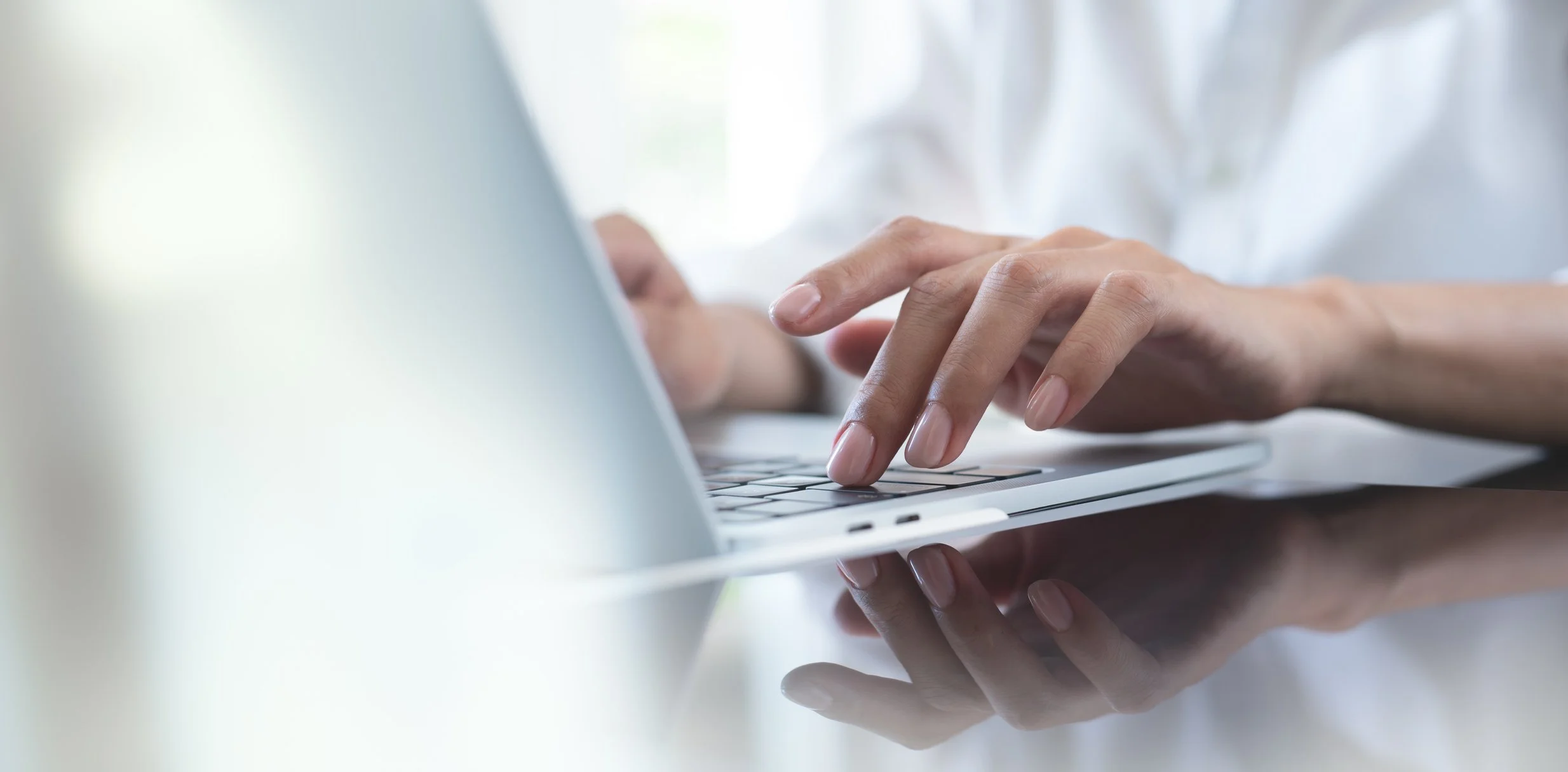 Person typing on a laptop keyboard with natural light in the background.