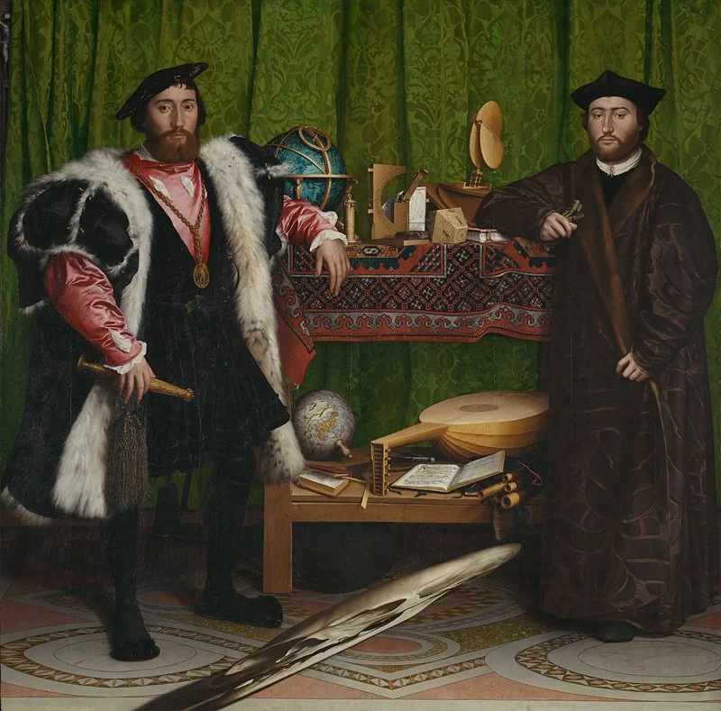Two men dressed in historical clothing from the Renaissance or early modern period, standing in front of a green curtain. The man on the left wears a fur coat, a hat, and holds a scepter; the man on the right wears a dark robe and hat. Between them are tables with scientific and musical instruments, globes, books, and scrolls.