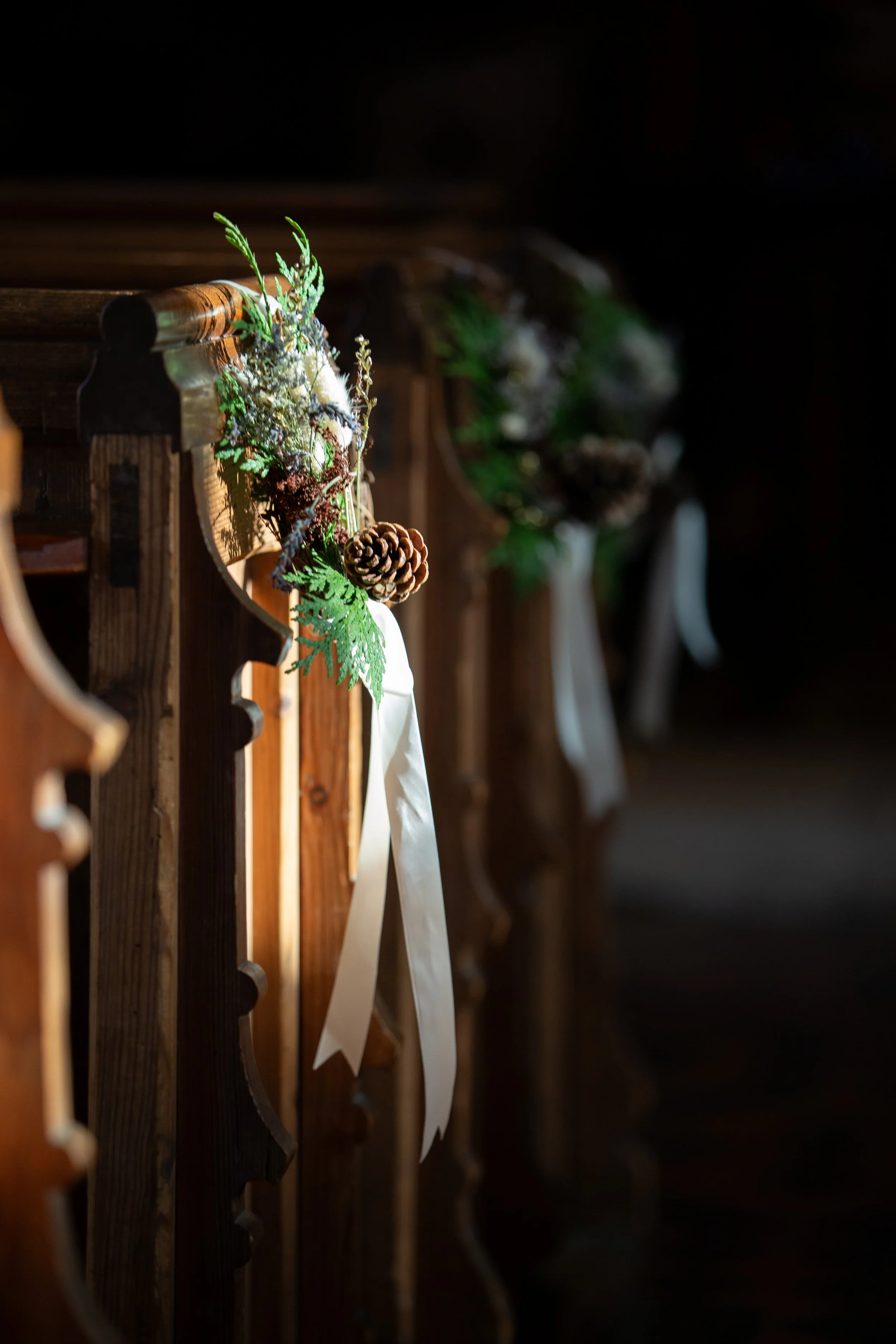 Wooden pews decorated with greenery and pinecones in a dimly lit church.