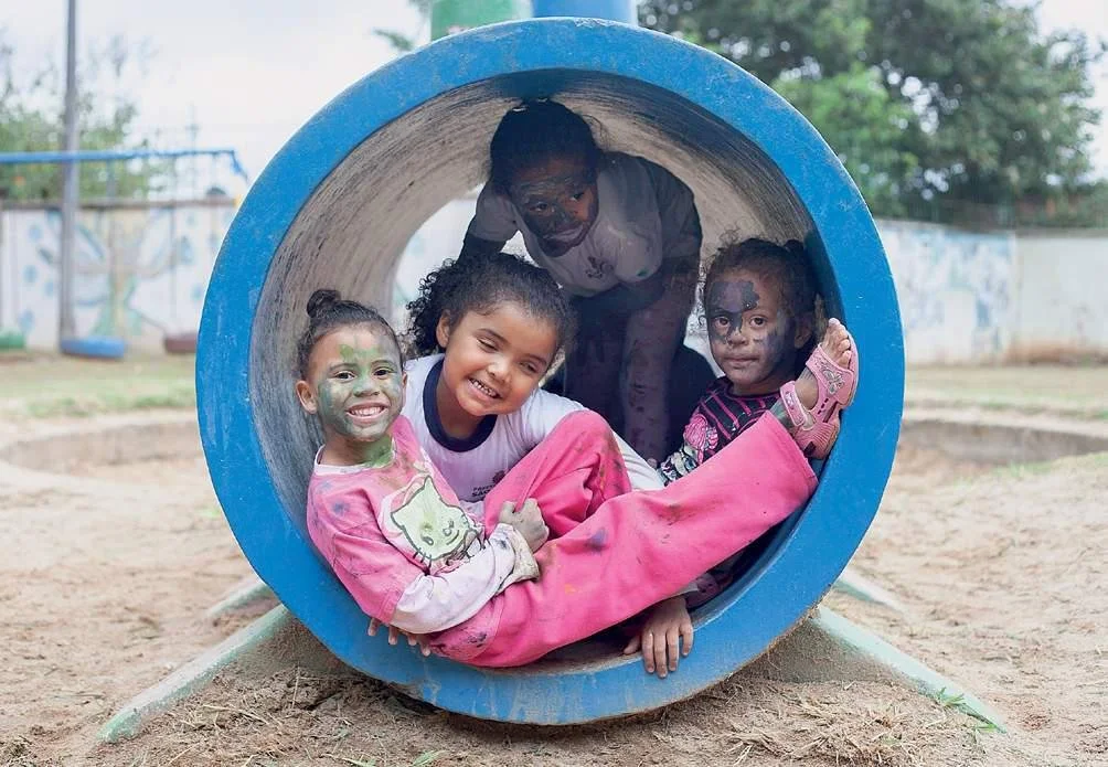 Four girls inside a big tube on a playgroung. They smile to the camera. They have their faces painted with ink.