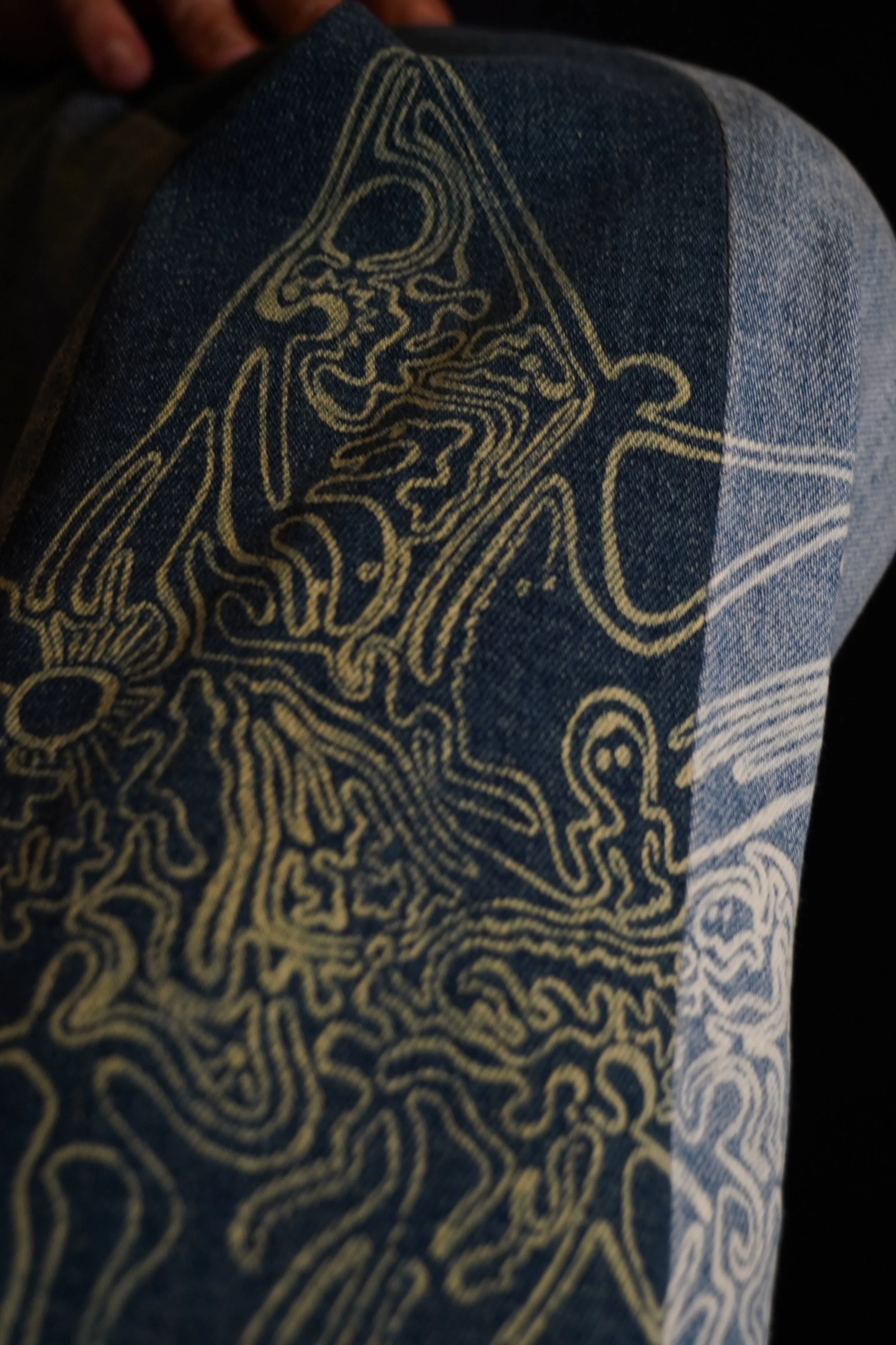 Close-up of a denim fabric with gold-colored embroidery forming an intricate, abstract design.