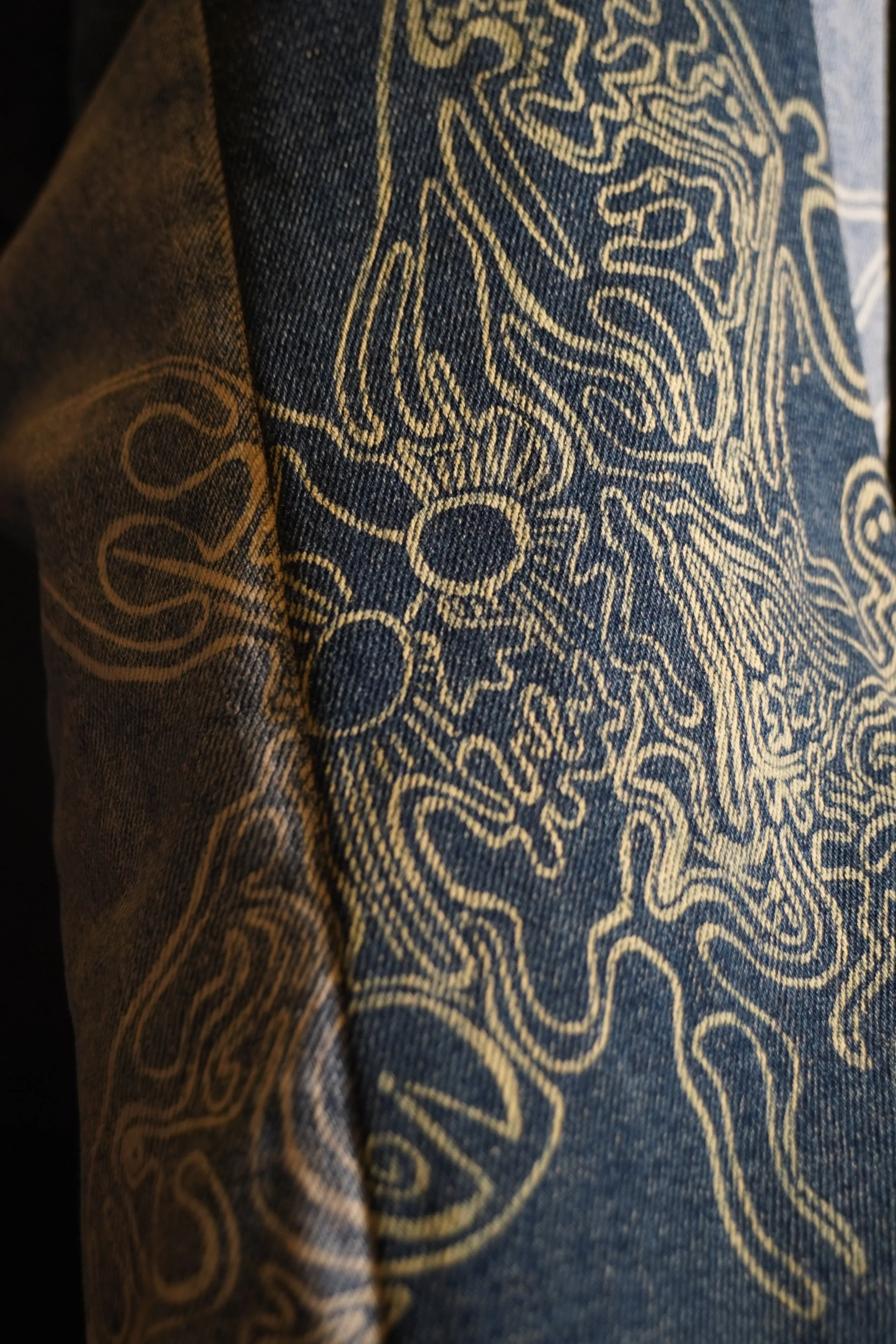 Close-up of dark fabric with a golden, intricate, abstract pattern.