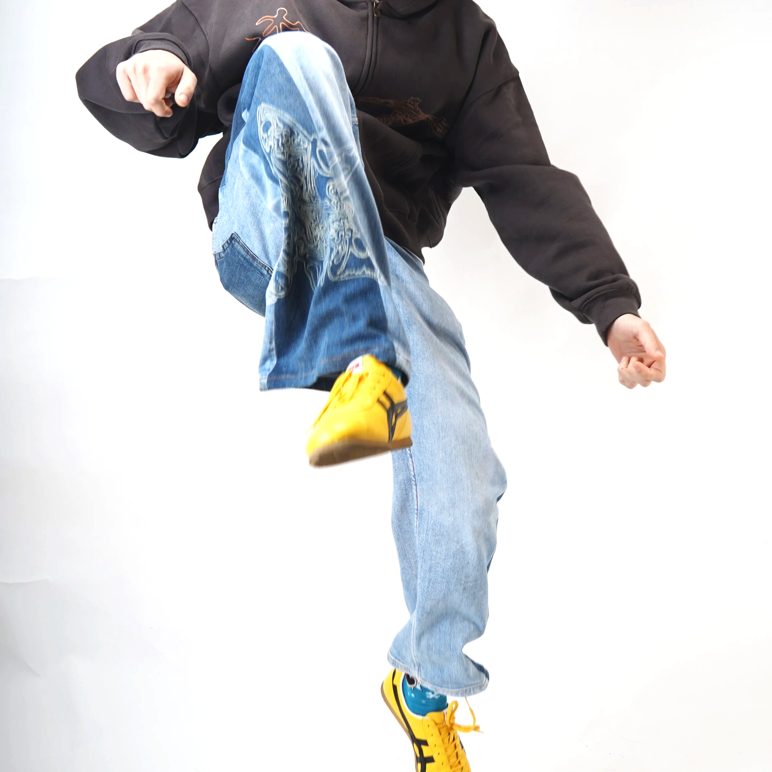 A person wearing a black hoodie, light blue jeans, and yellow sneakers, captured mid-move against a plain white background.