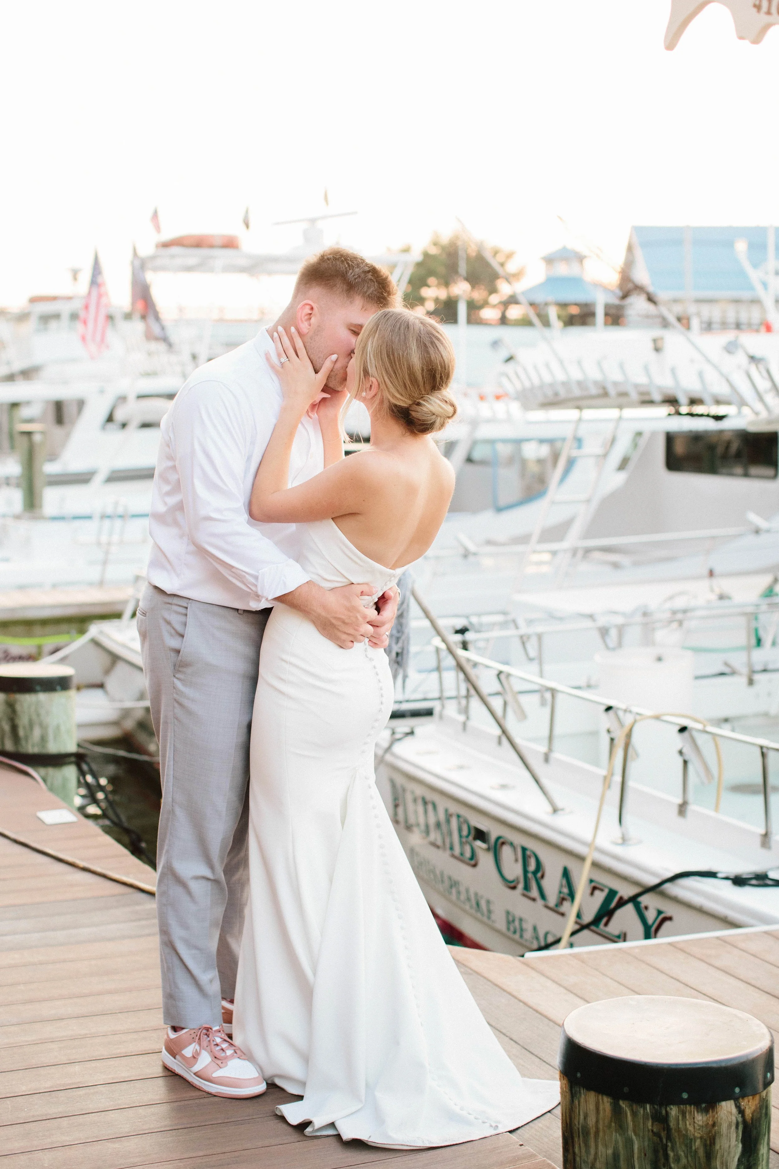A couple in wedding attire sharing a kiss on the docks of Rod 'N' Reel Marina with boats in the background.