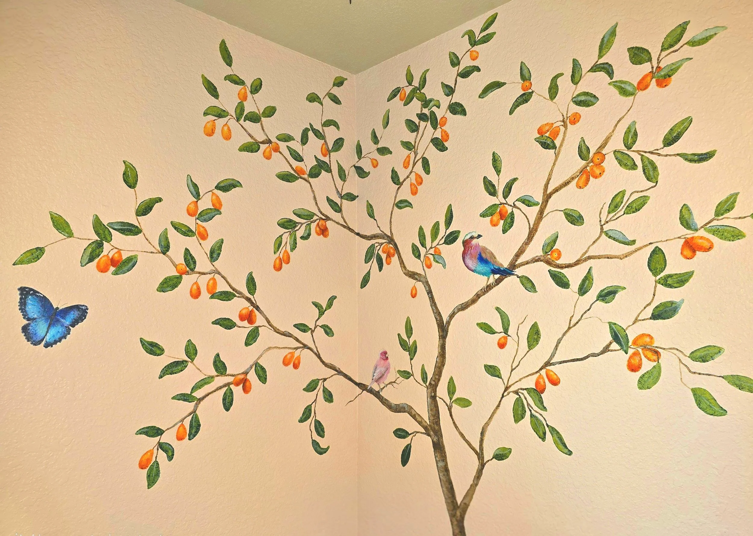 Wall painting of a tree with green leaves and orange fruits, featuring a blue butterfly and three colorful birds perched on its branches.