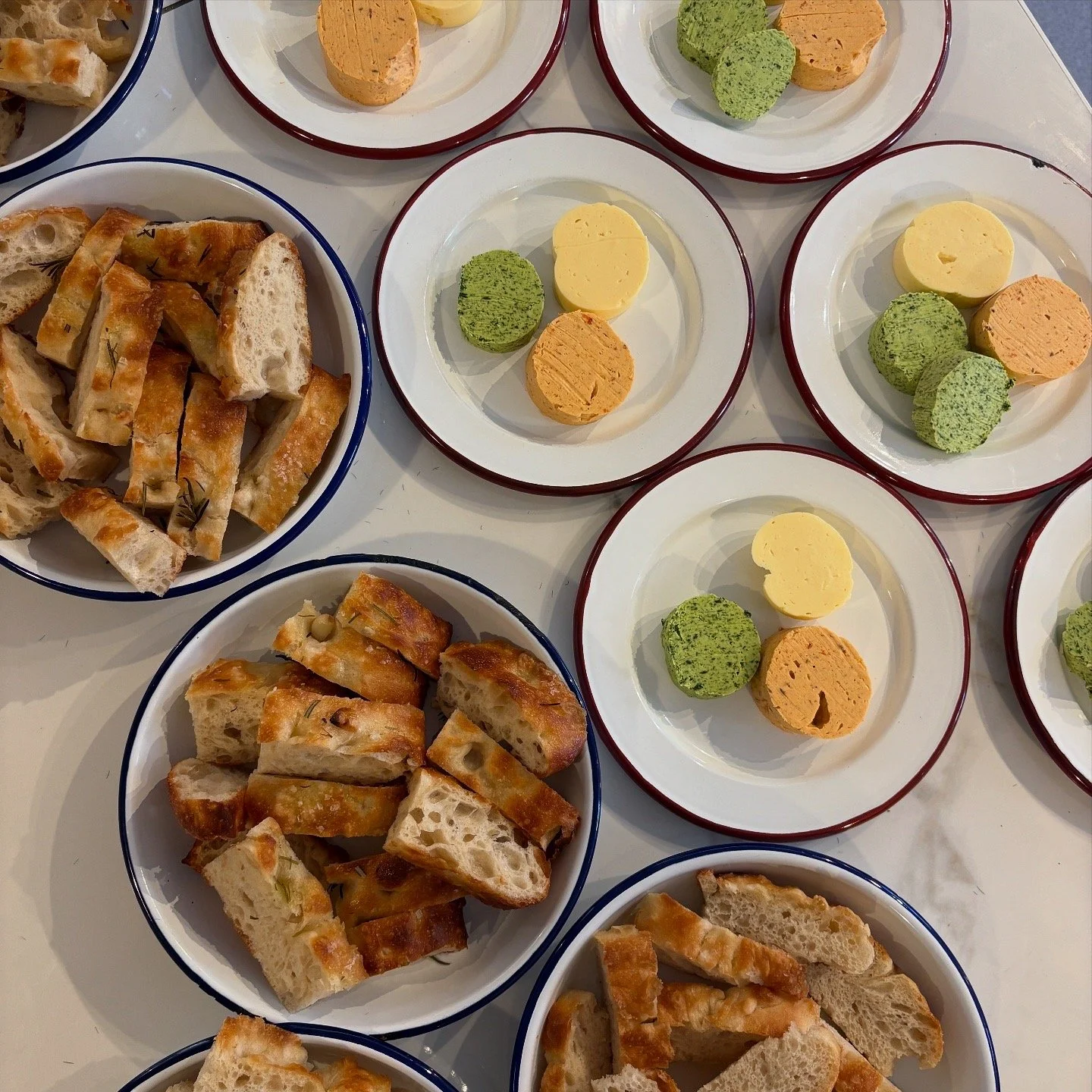 Plates of assorted bread slices and cheese rounds on a white table.