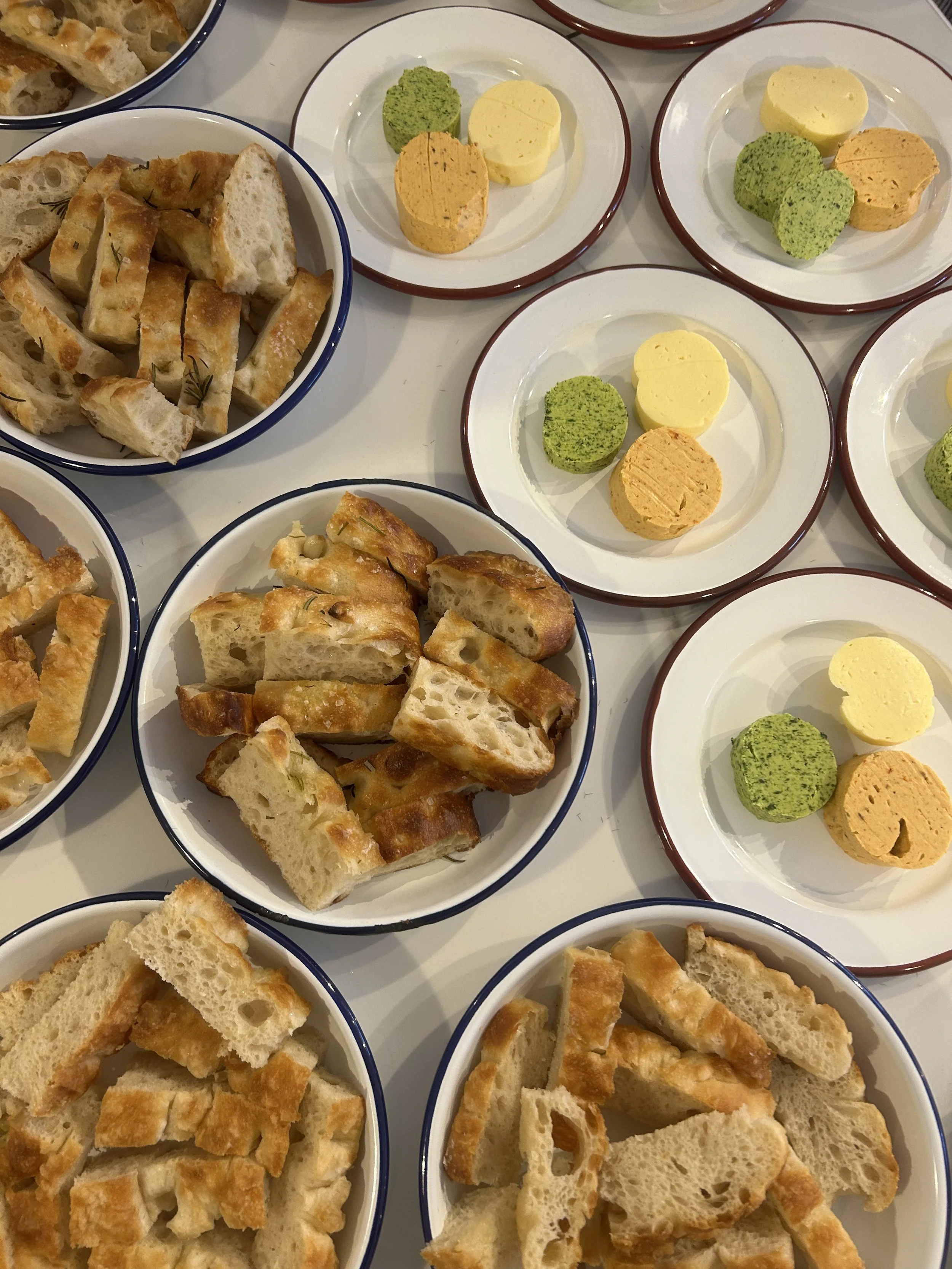 Several plates of sliced bread and small plates of assorted pâté or spreads, some green and some yellow, arranged on a white surface.