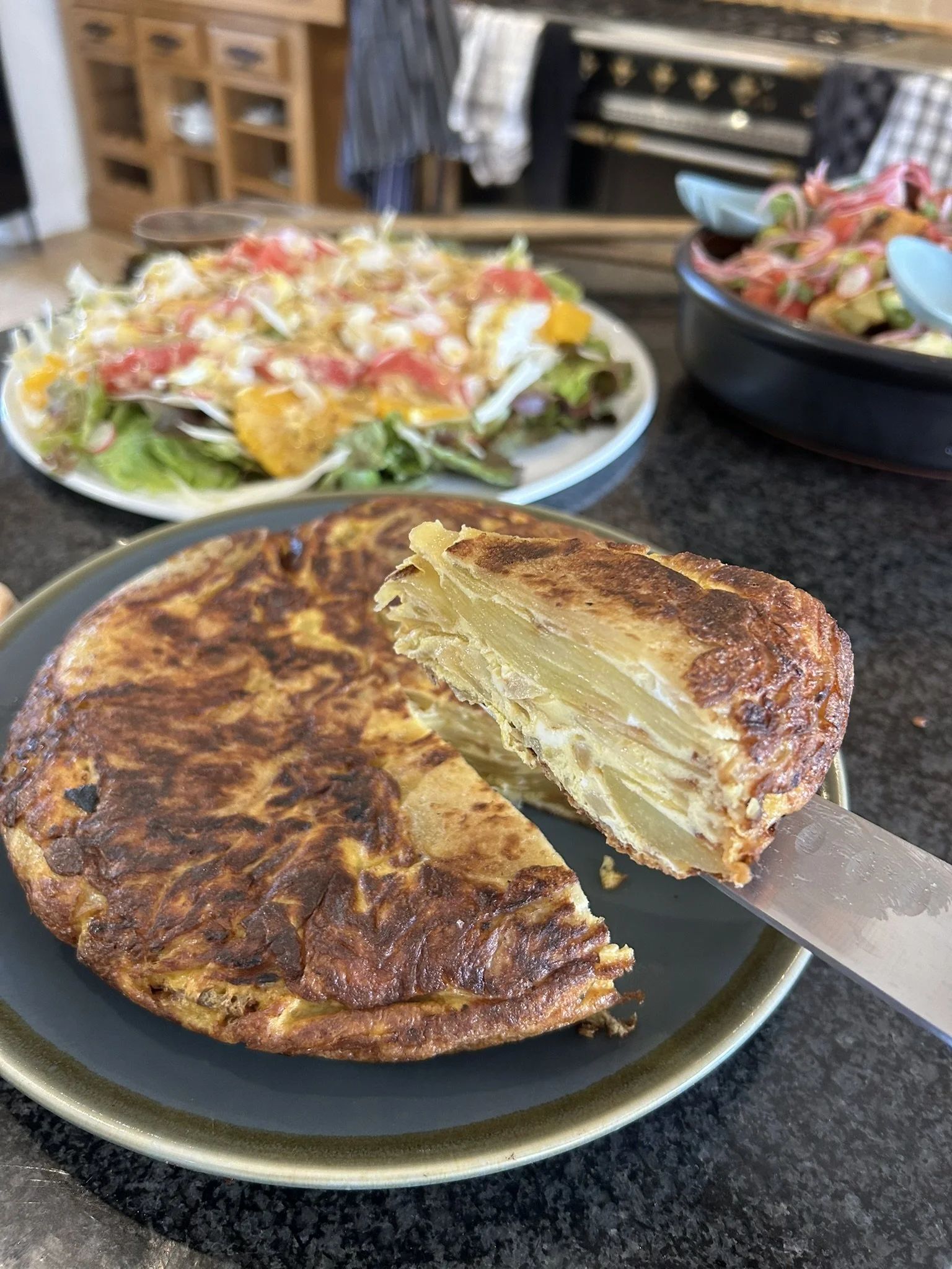 A Spanish tortilla with sliced potatoes and eggs on a blue plate, with a piece cut out showing layers of potatoes inside.