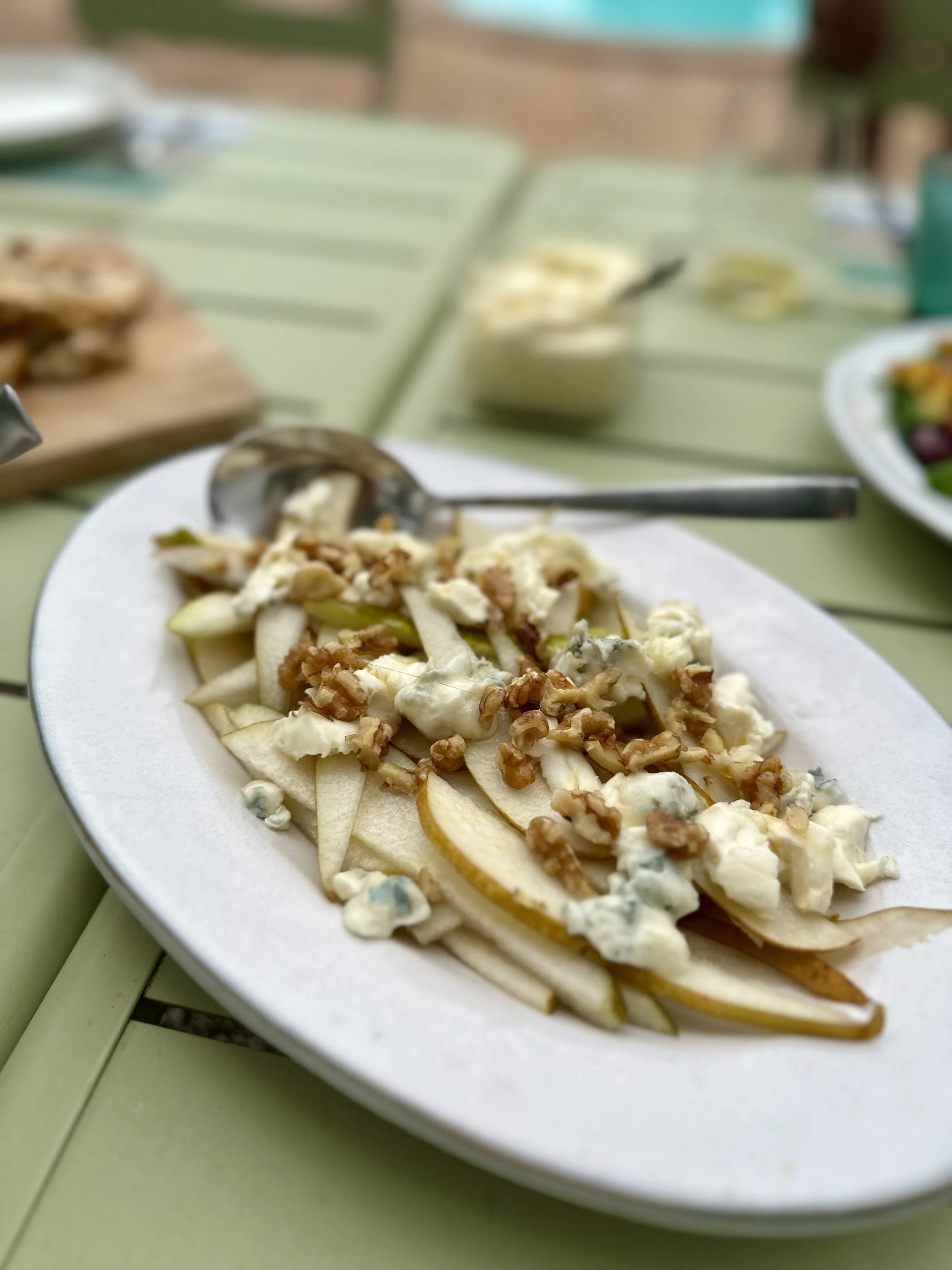 A white oval plate with pear slices, crumbled blue cheese, walnuts, and a creamy dressing on a light green table.