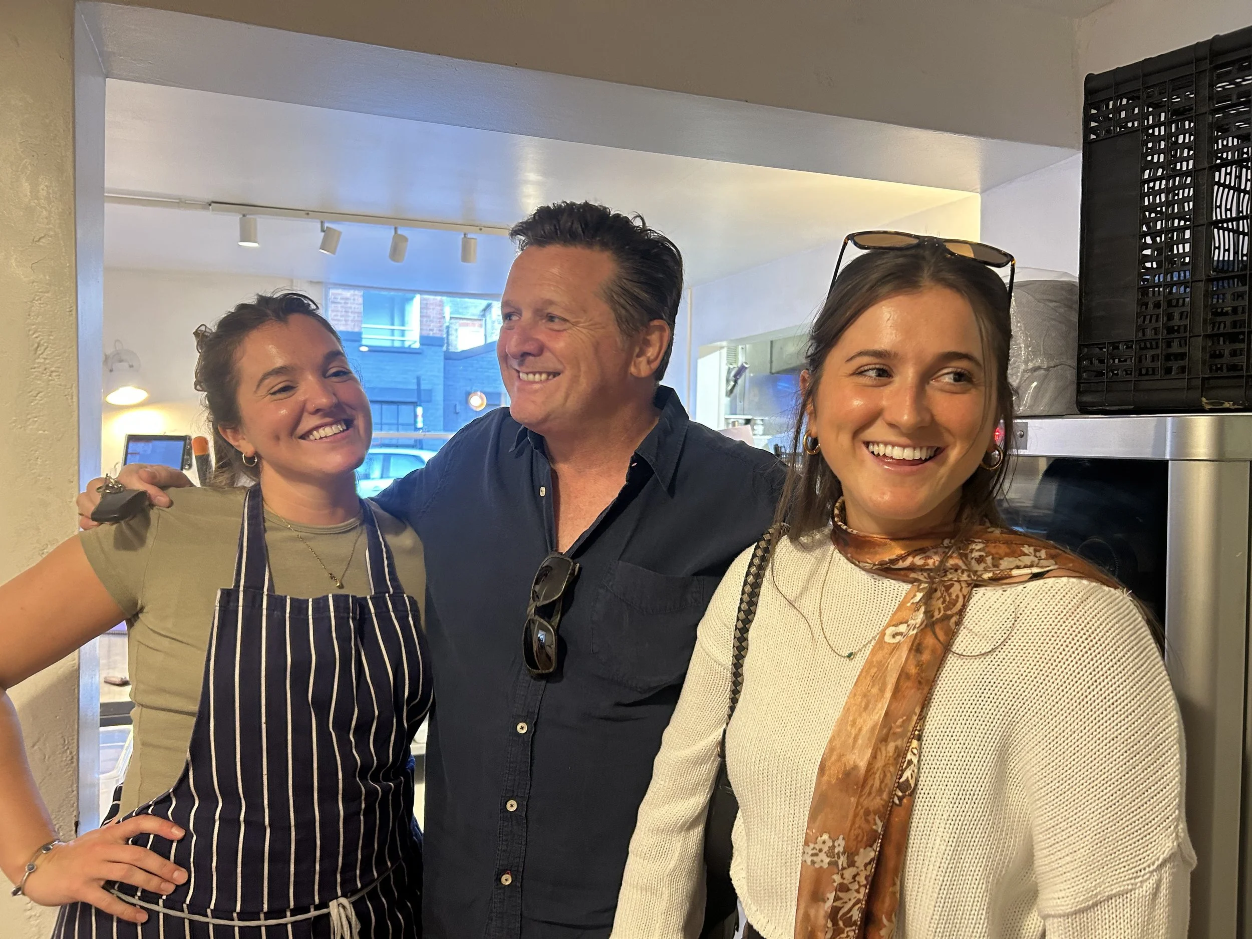 Three people smiling and posing together inside a restaurant or cafe.