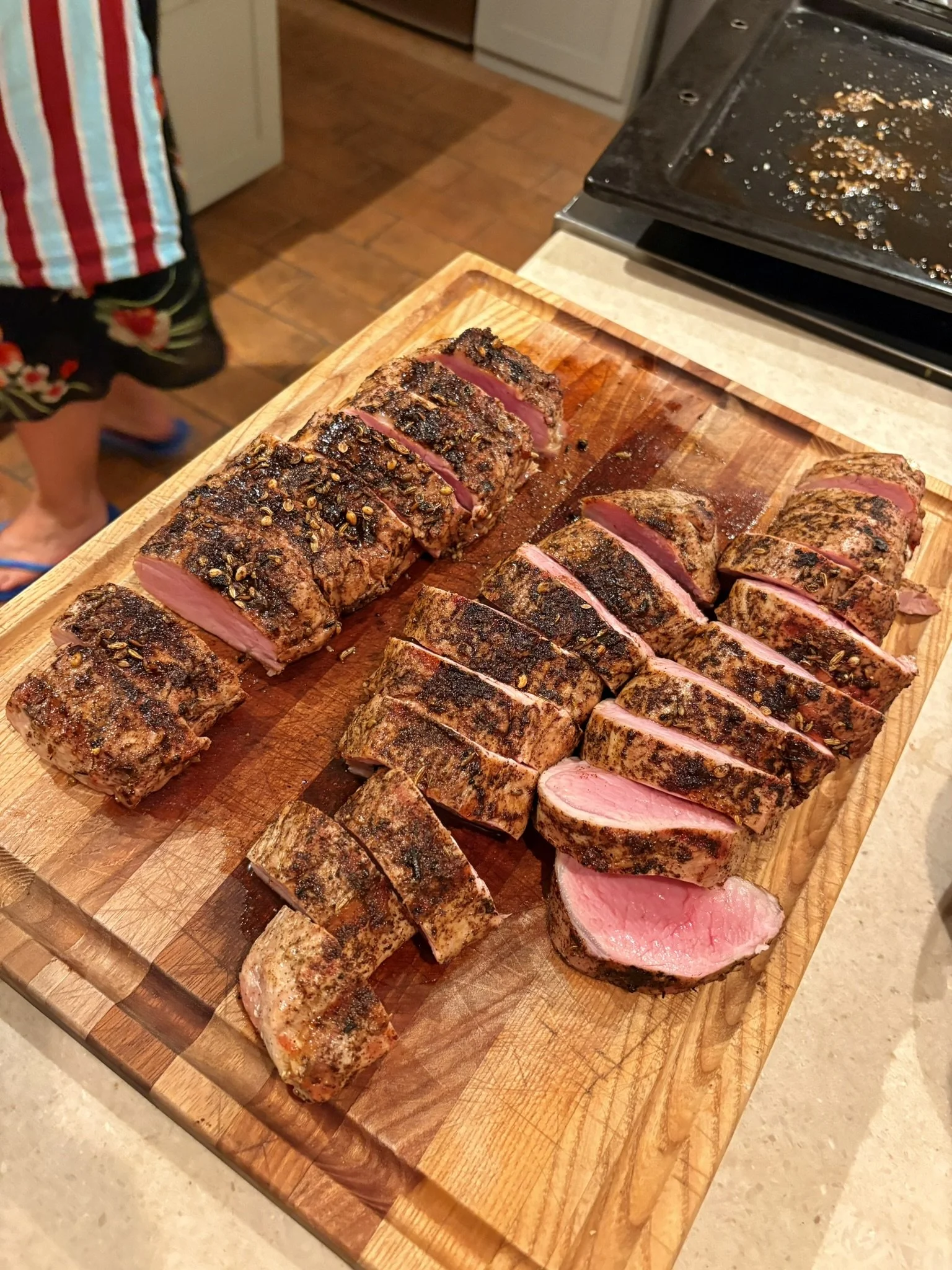 Plate of sliced, grilled beef tenderloin on a wooden cutting board in a kitchen.