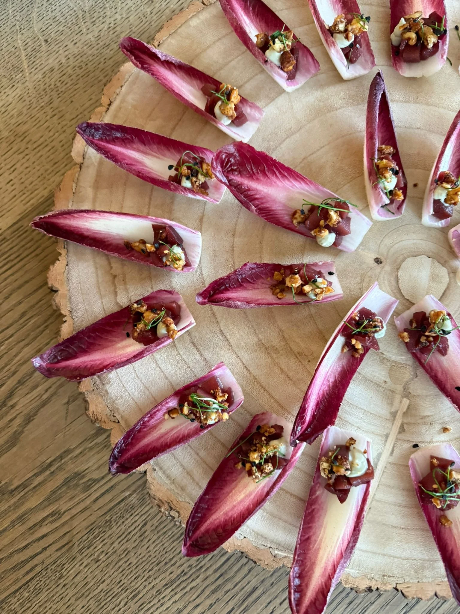 Radicchio leaf canapés topped with cheese, diced meat, microgreens, and crunchy nuts on a wooden serving board.