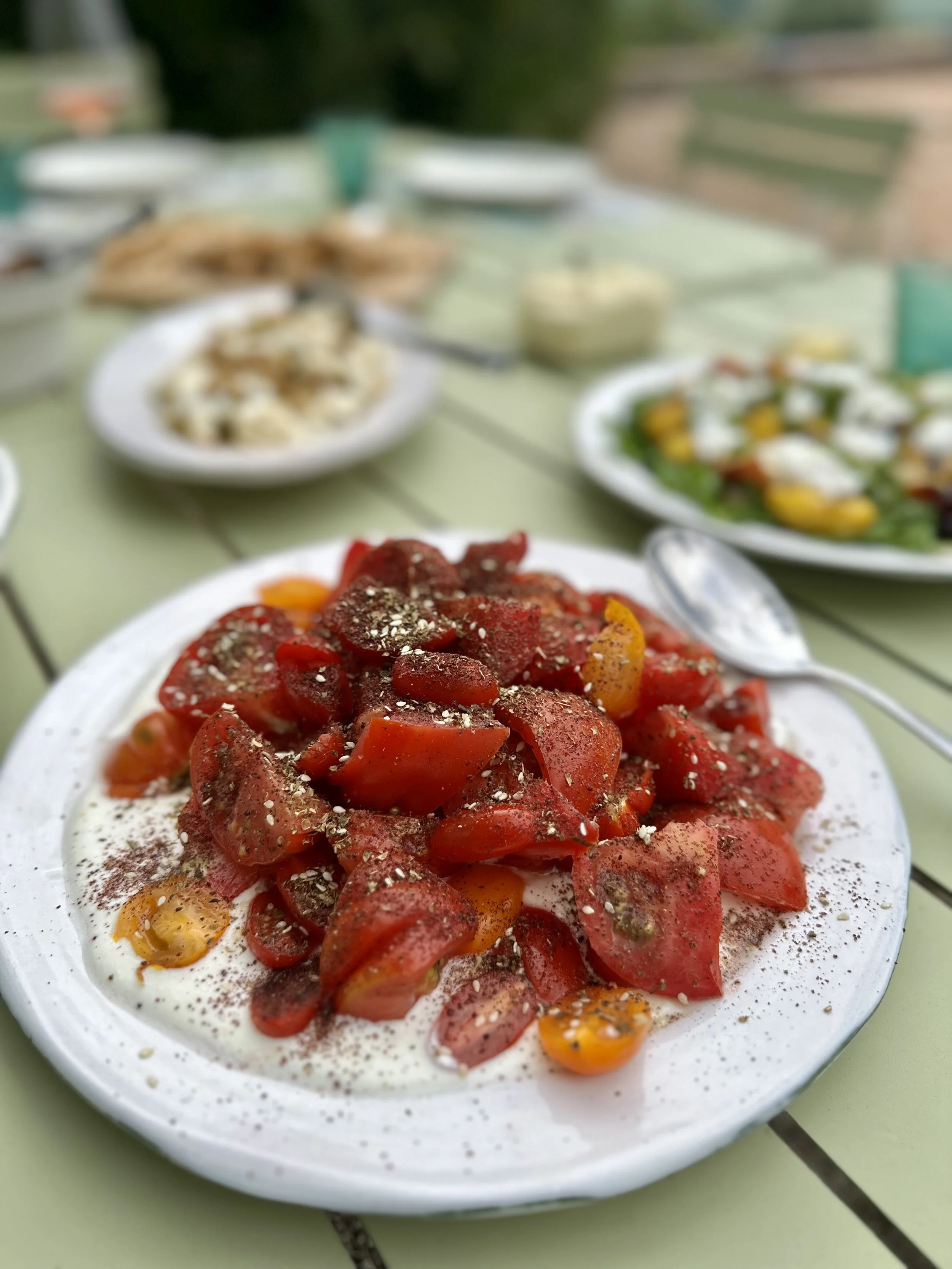Plate of salad with chopped tomatoes, sprinkled with black pepper and herbs, on a green outdoor table.