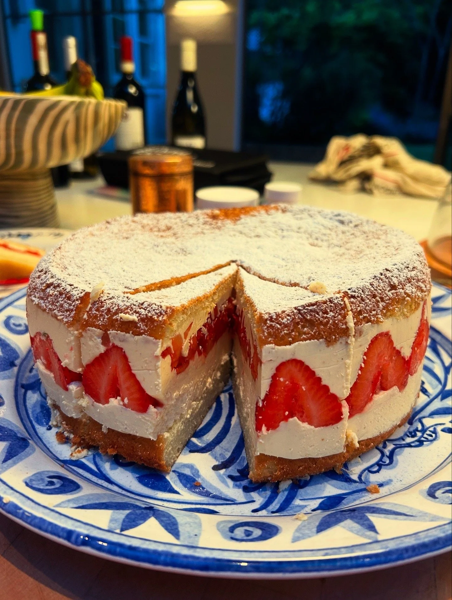 A partially sliced strawberry shortcake on a decorative blue and white plate, with layers of cream, strawberries, and cake.