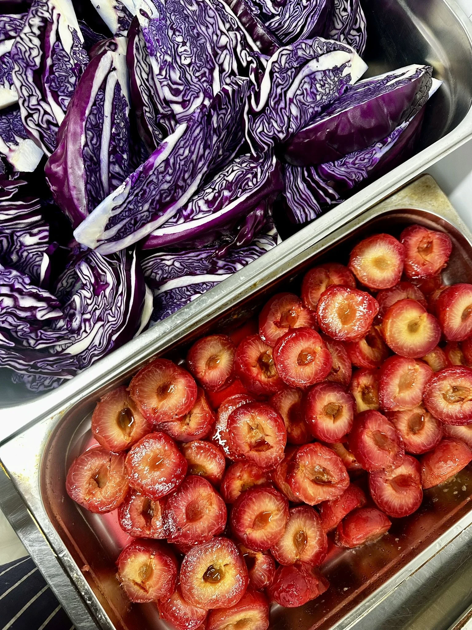 Chopped red cabbage and strawberries in separate stainless steel containers.