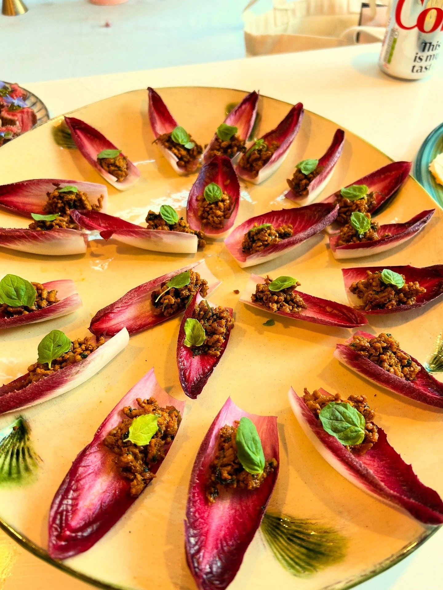 Radicchio leaf cups filled with a ground meat mixture, garnished with small basil leaves, arranged on a yellow plate.