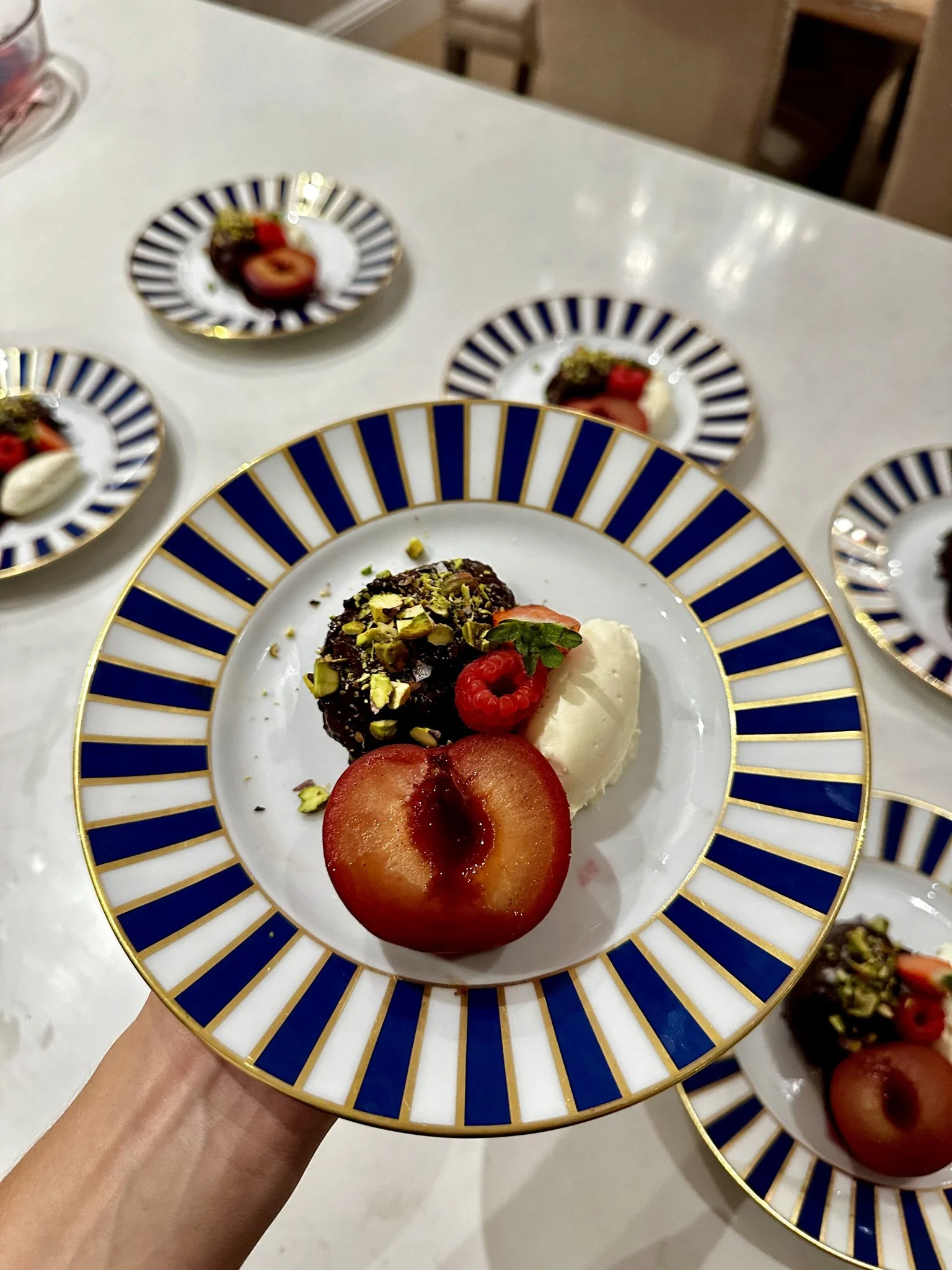 Close-up of a decorative plate with a baked apple, a scoop of ice cream topped with pistachios, and garnished with a raspberry and a mint leaf, with other similar plates in the background.