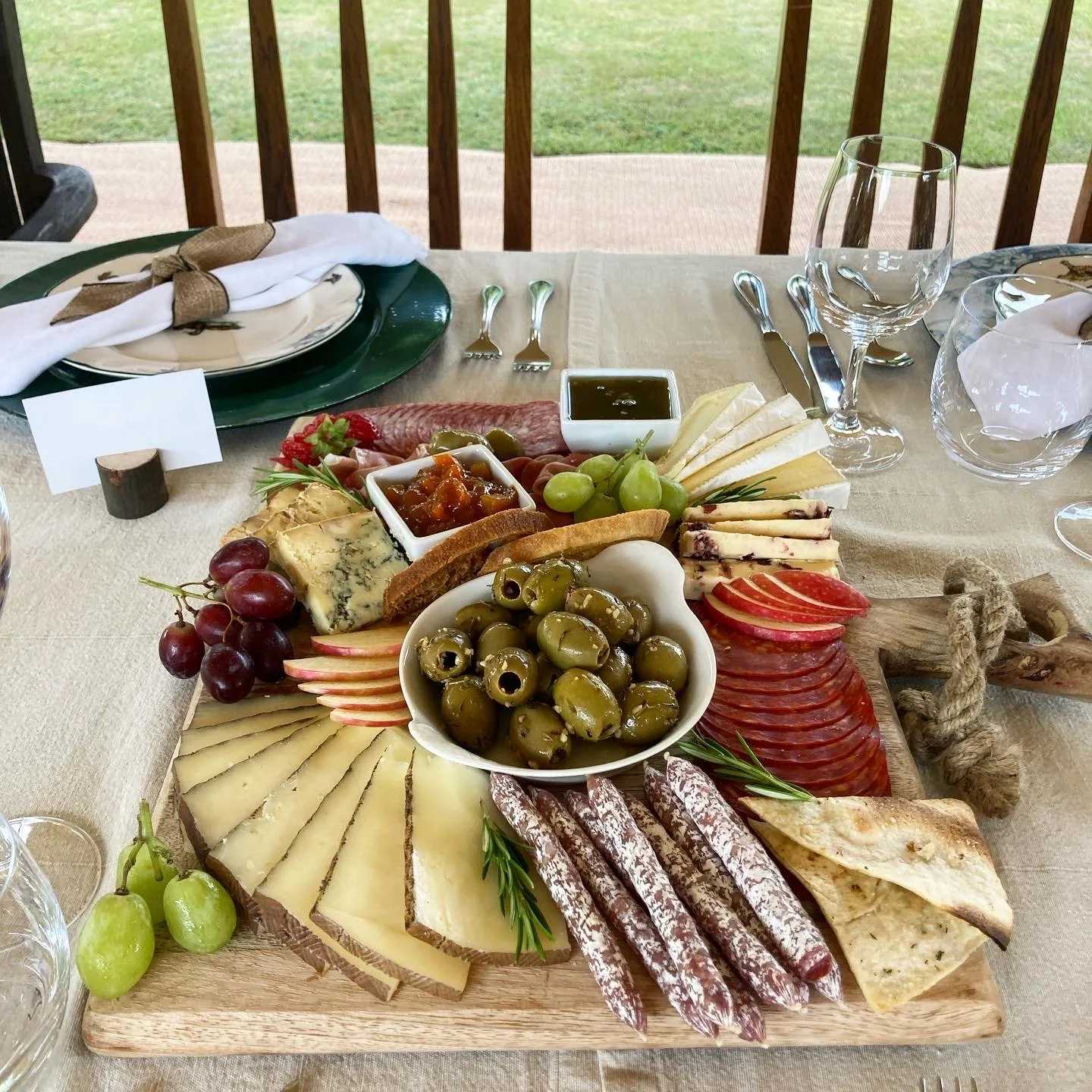 Cheese, grapes, olives, cured meats, and spreads on a wooden cheese board for a charcuterie presentation.