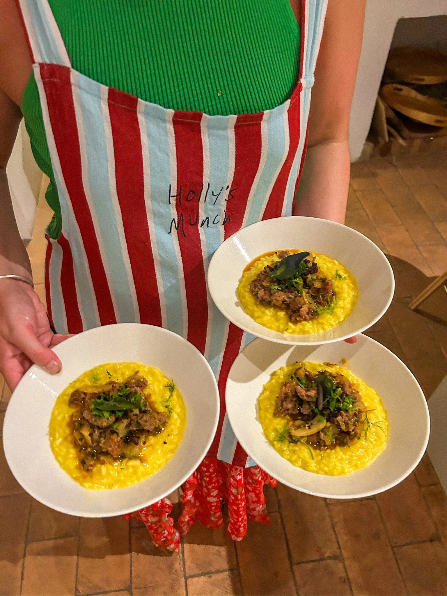 Person holding three plates of yellow rice with meat and herbs, wearing a striped apron with 'Holly's Munch' written on it.