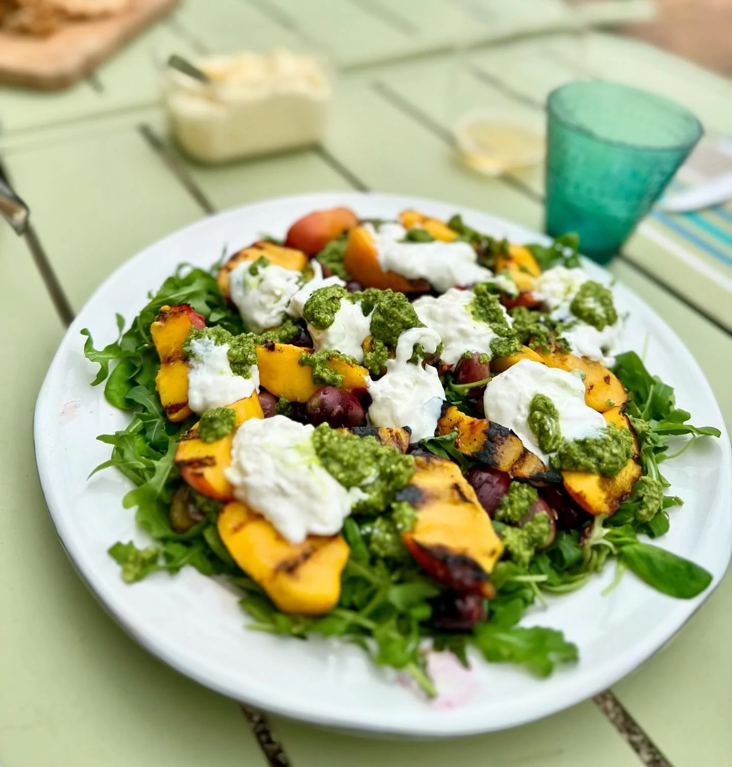 A plate of grilled peach and cherry salad topped with dollops of cheese and green pesto.
