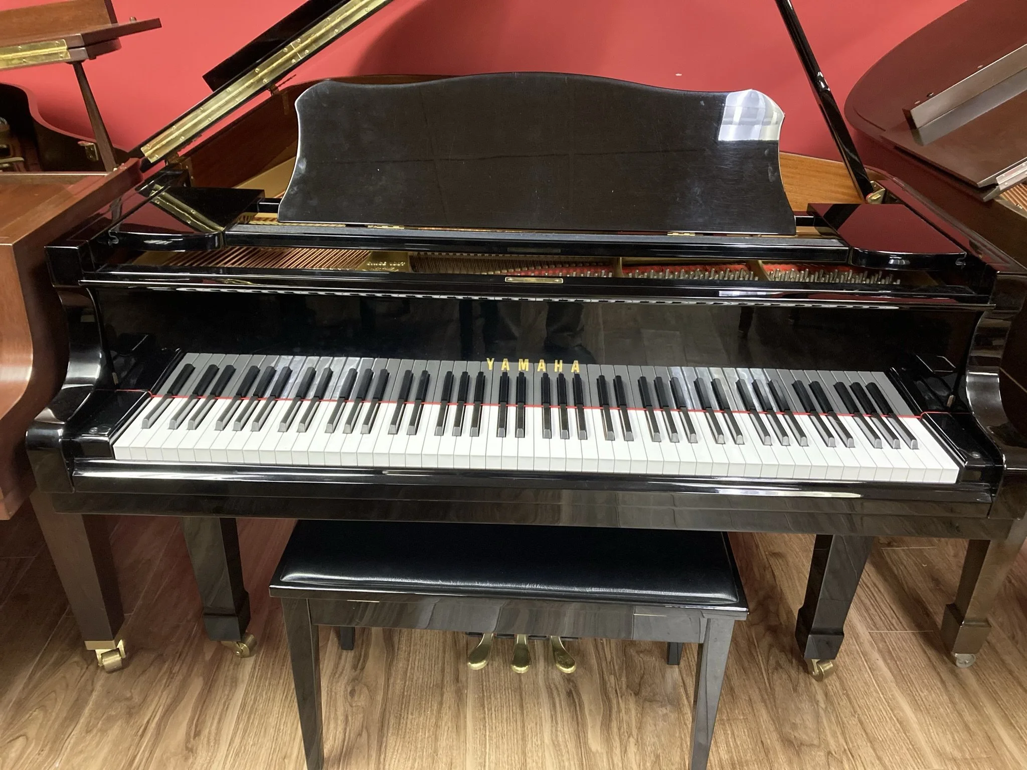 Black Yamaha grand piano with open lid and visible piano keys, placed on a wooden floor with a piano bench.