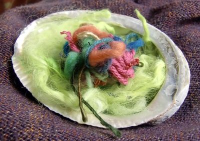 Close-up of a green seashell filled with colorful yarn and fibers on a dark surface.