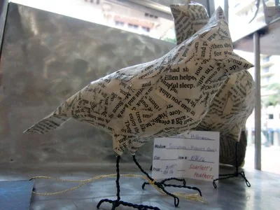 Handmade bird sculpture wrapped in newspaper with wire legs and tail.