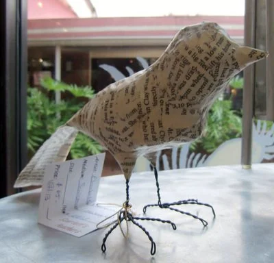 Paper bird sculpture with wire legs on a white table near a window