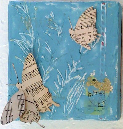 Mixed media art with blue background, white painted branches, and cut-out paper butterflies made from sheet music.