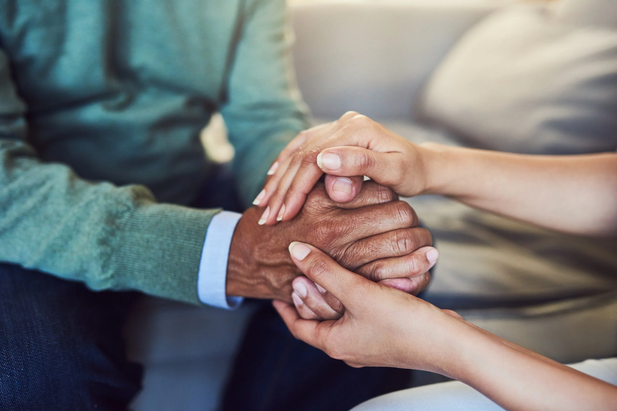 Close-up of two people holding hands, one with darker skin and the other with lighter skin, conveying support or comfort.