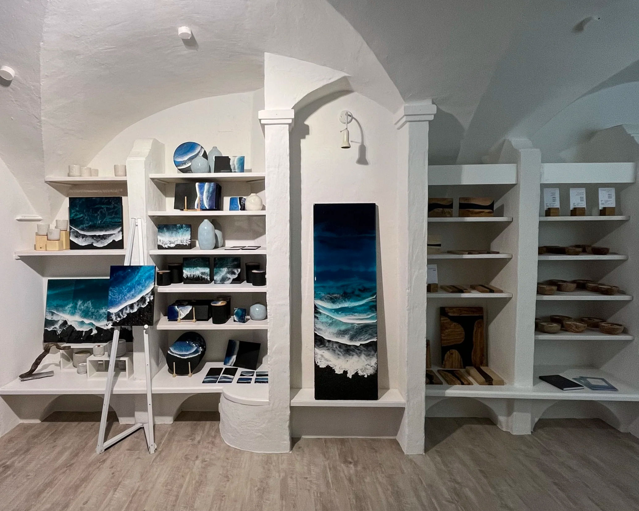 Kunstgalerie mit Meeresbildern auf Regalen und auf Leinwand, Skulpturen, Holzarbeiten, und Verkaufsdisplays in weißem Raum.