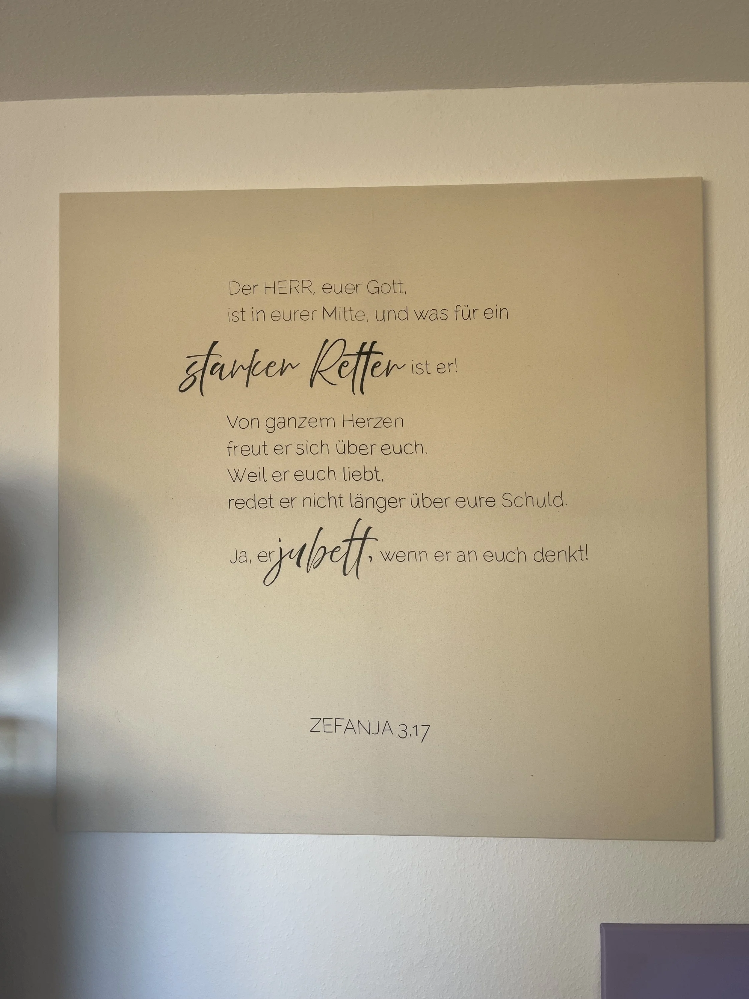 Ein christliches Zitat auf einer Wandtafel, das Gott in der Mitte lobt und über einen starken Retter spricht, mit einer Bezugnahme auf die Bibelstelle Zefanja 3:17.
