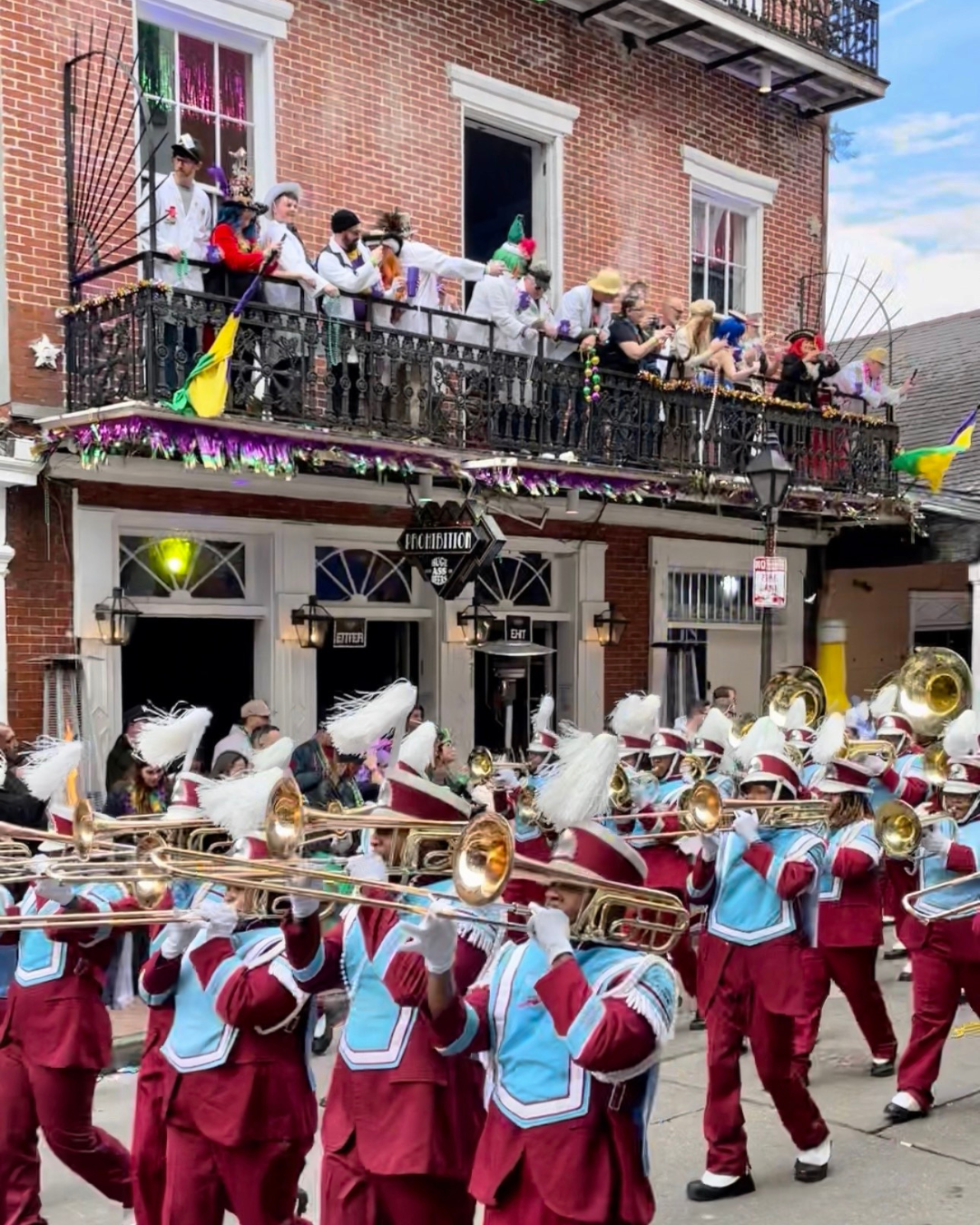 Warren Easton High marching band parades during Mardi Gras as people watch from the balcony
