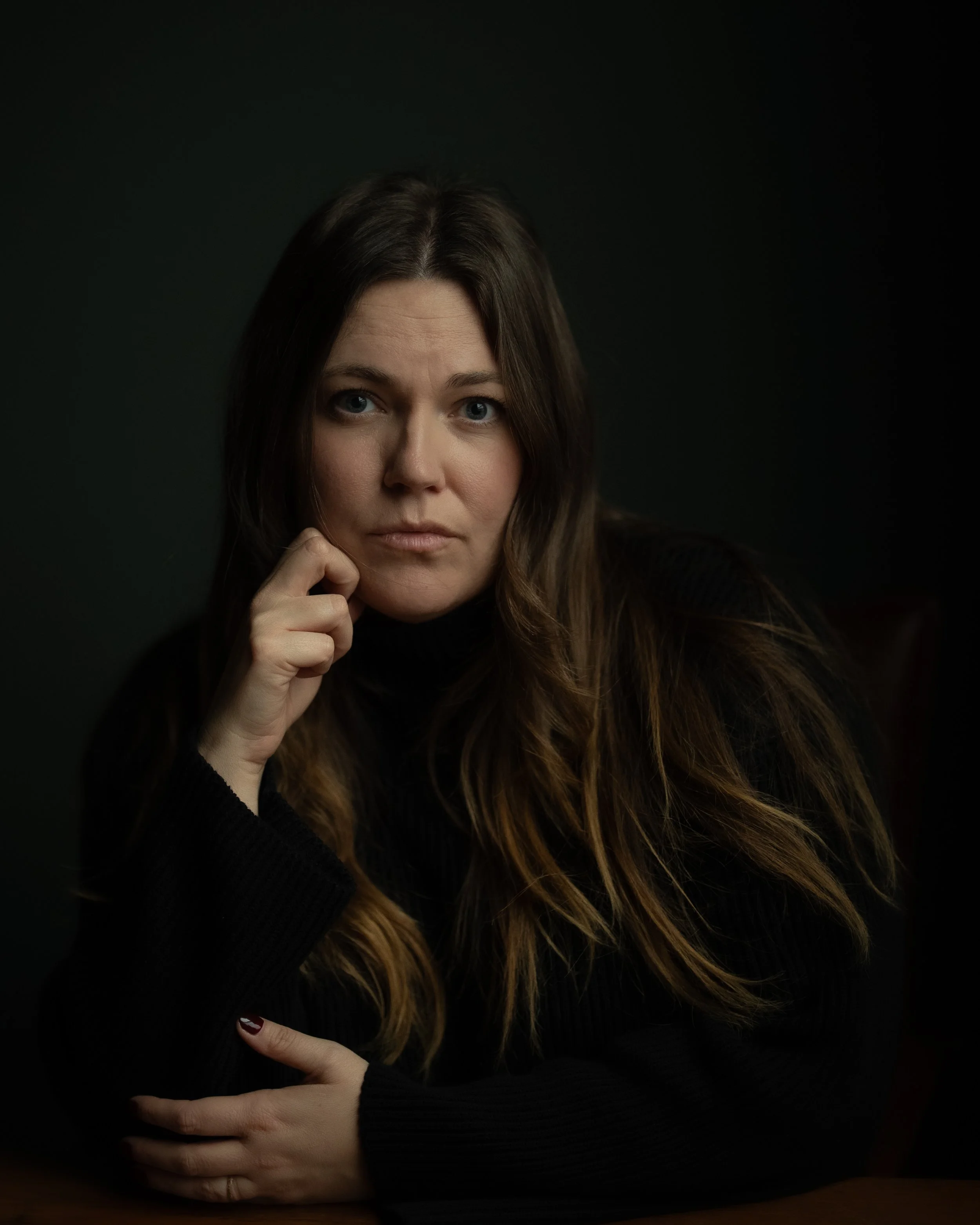 brown haired woman in black sweater staring at camera with hand on chin