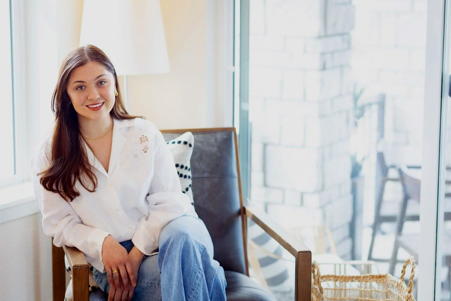 brunette woman smiling, sitting in chair in bright naturally lit room