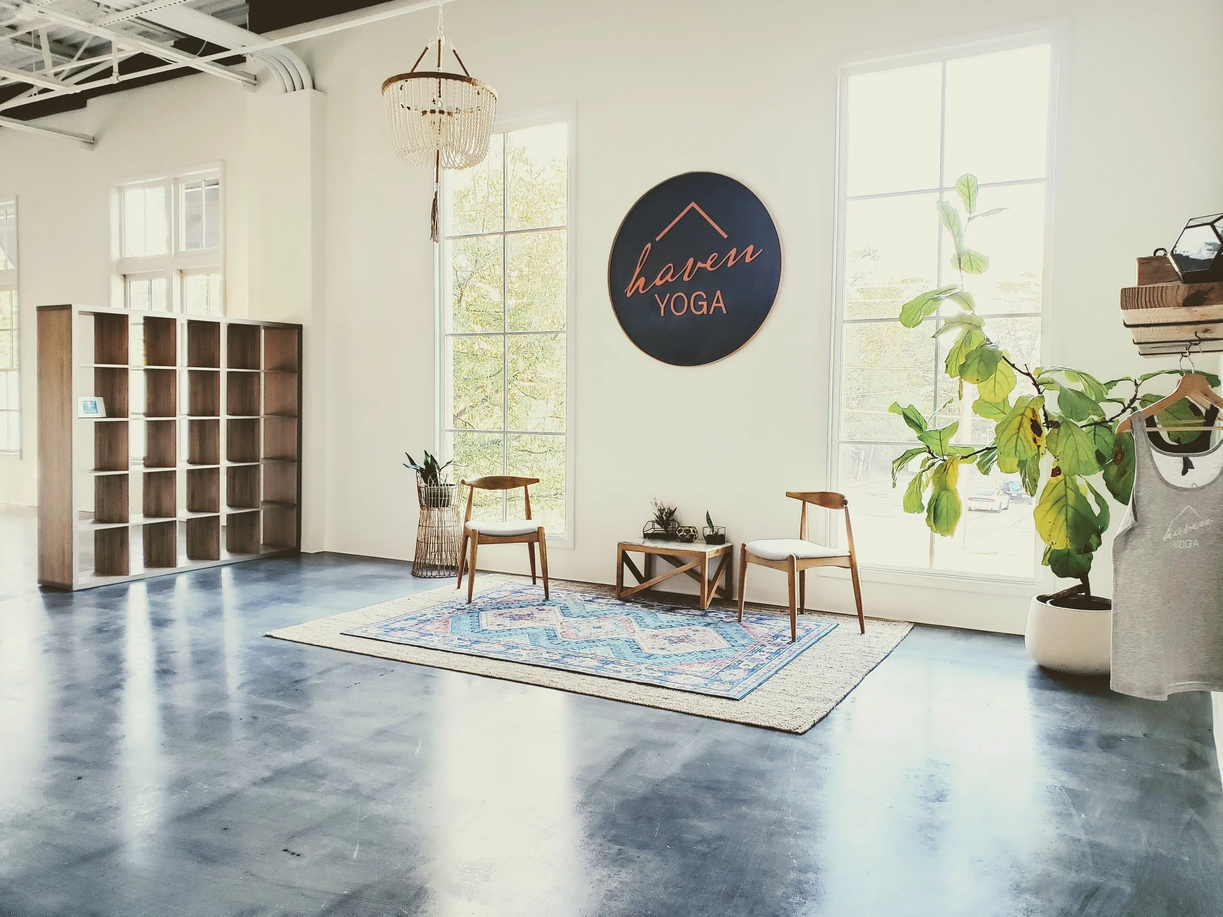 A minimalist yoga studio with wooden shelves, two chairs on a rug, a potted plant, and the words 'Haven Yoga' on the wall.