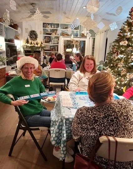 BAM! beginner Mahjong students playing together in San Diego at a Holiday Party in a room filled with Christmas decorations and tables of people playing Mahjong