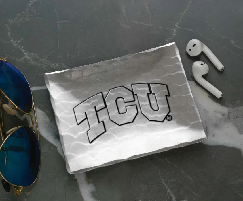 A paper napkin with Texas A&M University logo and name on a wooden table, with four quarters placed beside it.
