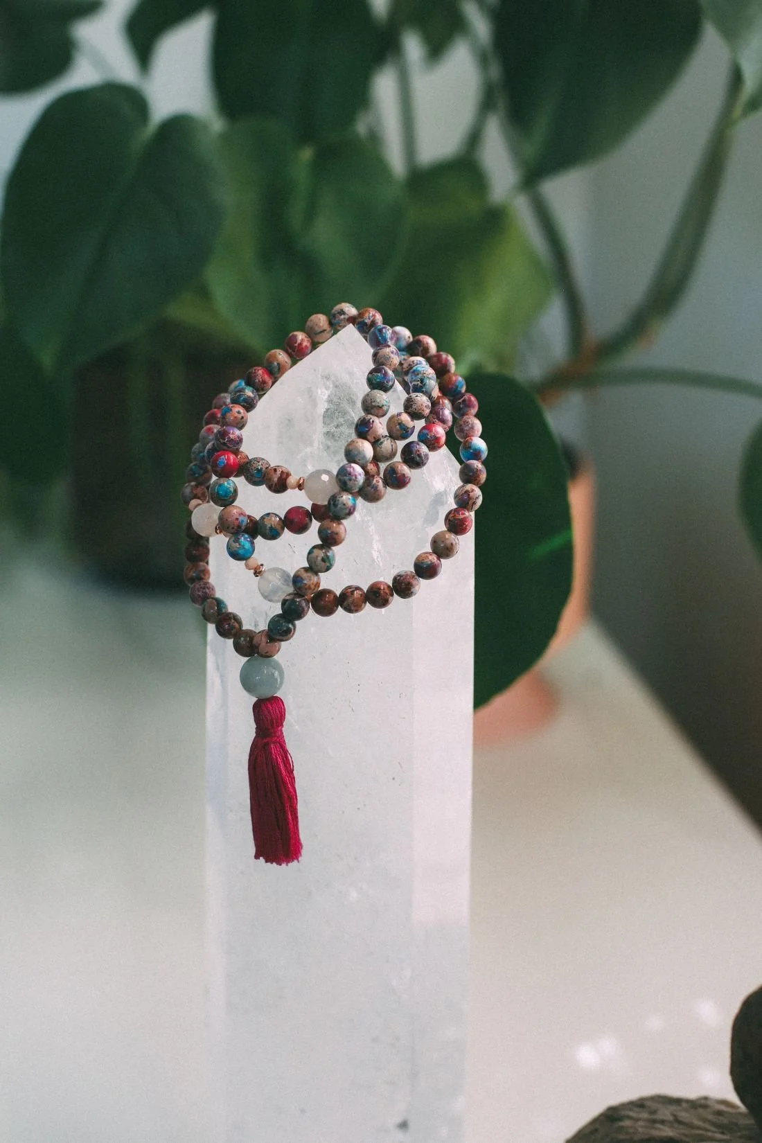 mala necklace draped over a white crystal green plant in background