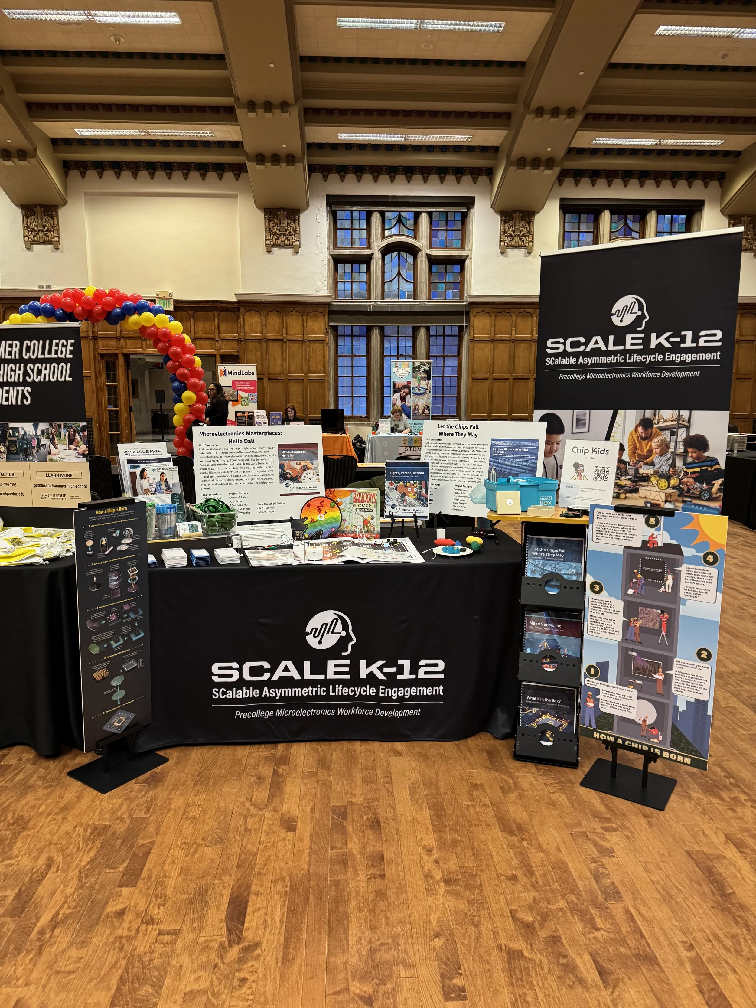 “A SCALE K‑12 booth displays program materials, banners, and posters in a large hall, with neighboring booths visible around it.”