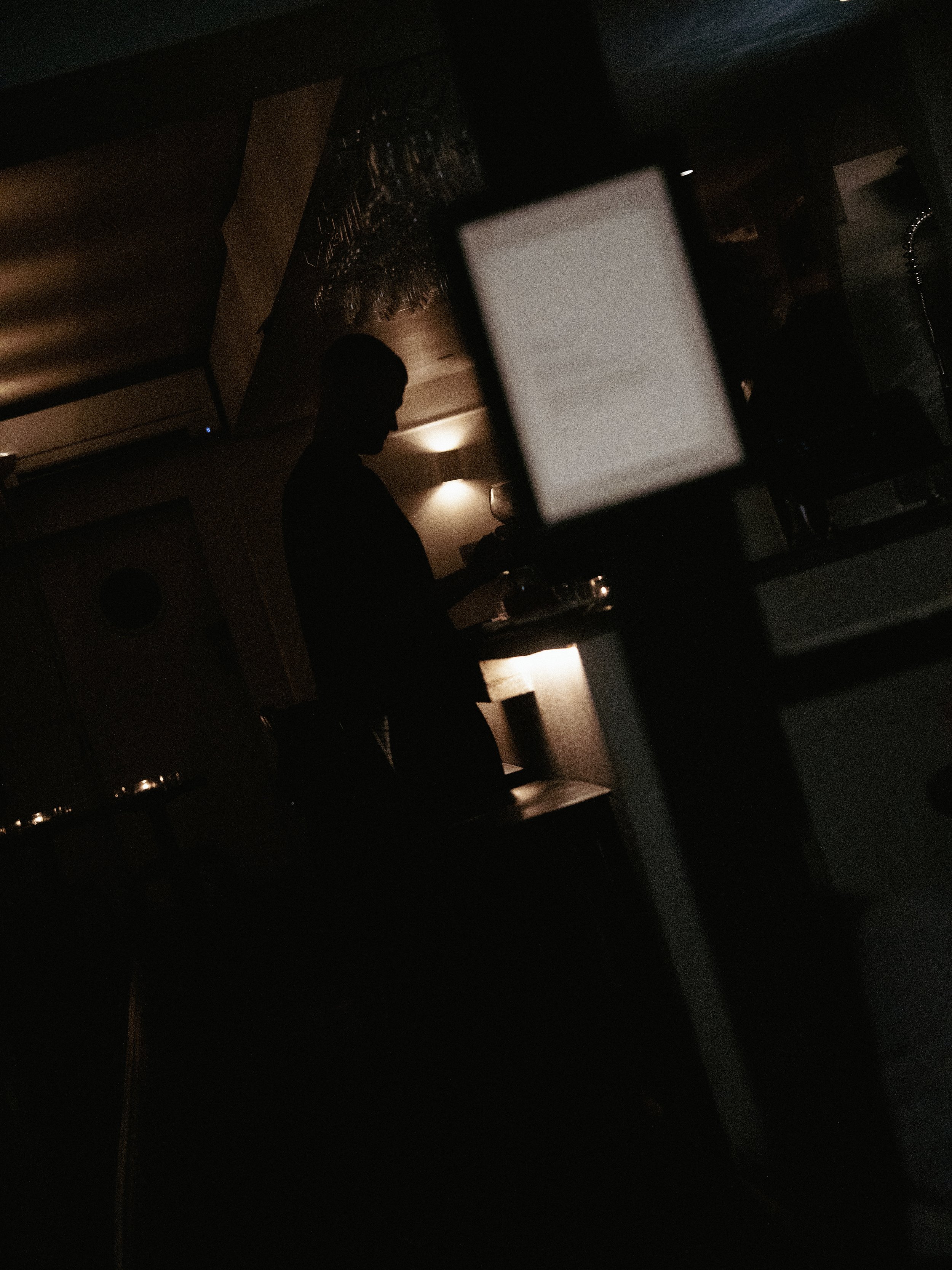 A dark room with a silhouette of a person holding a glass, illuminated by soft, warm lighting from the background.
